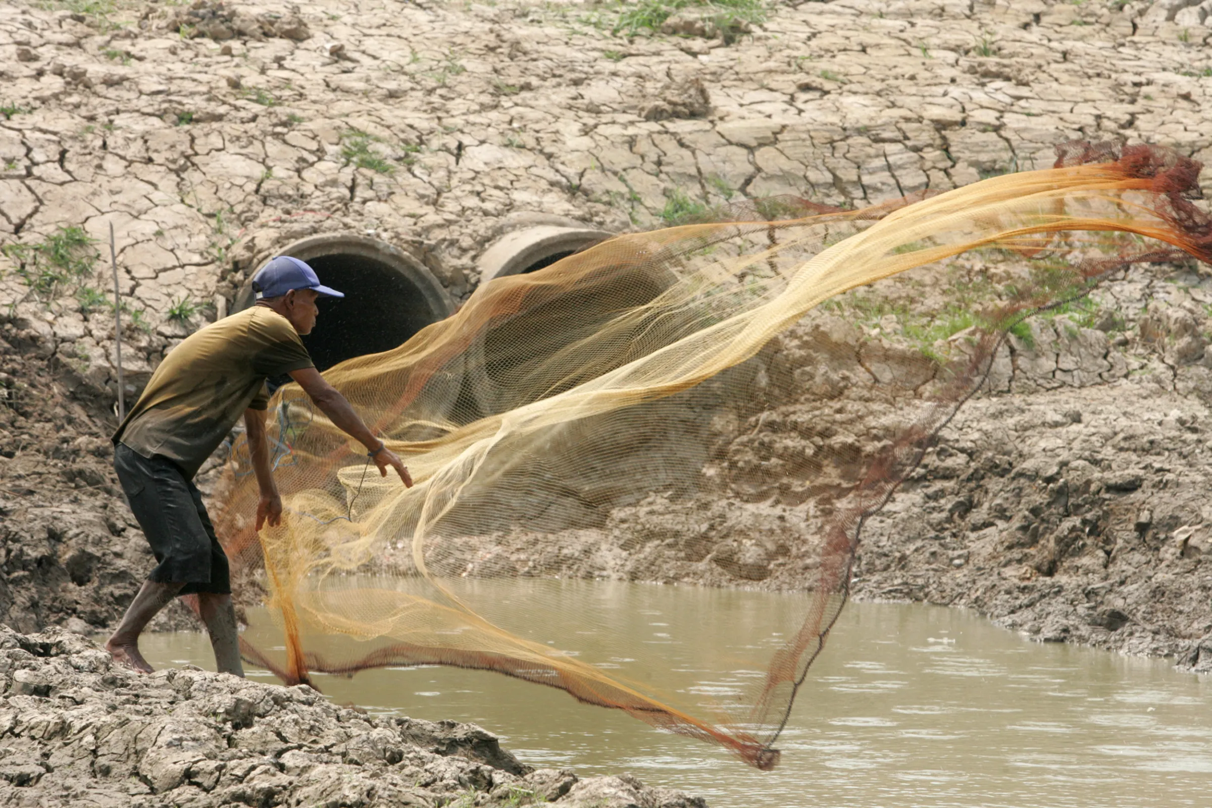 A Thai farmer casts his net in a parched irrigation canal in Thailand