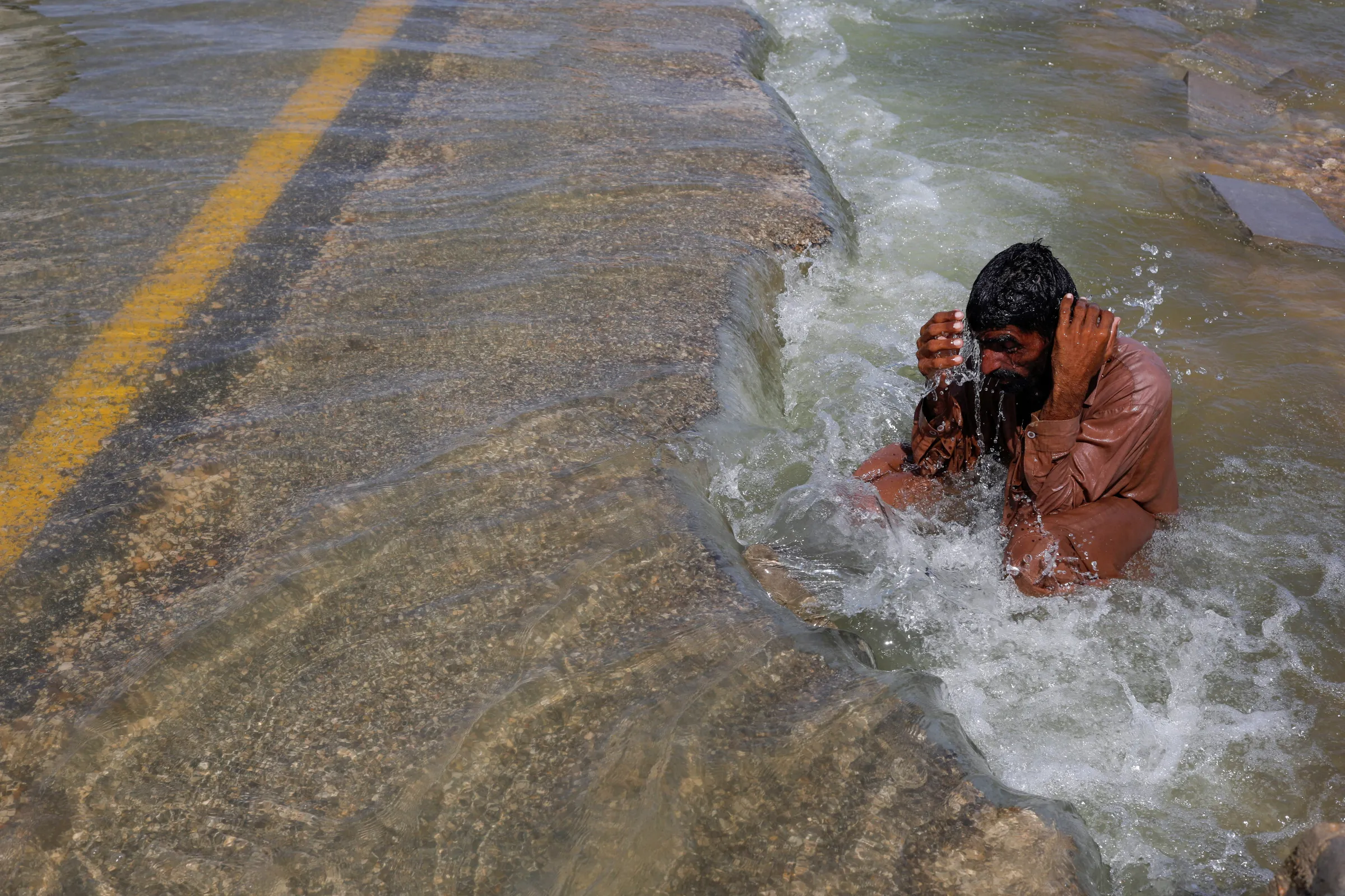 A displaced man cools off to avoid heat on flooded highway, following rains and floods during the monsoon season in Sehwan, Pakistan, September 16, 2022