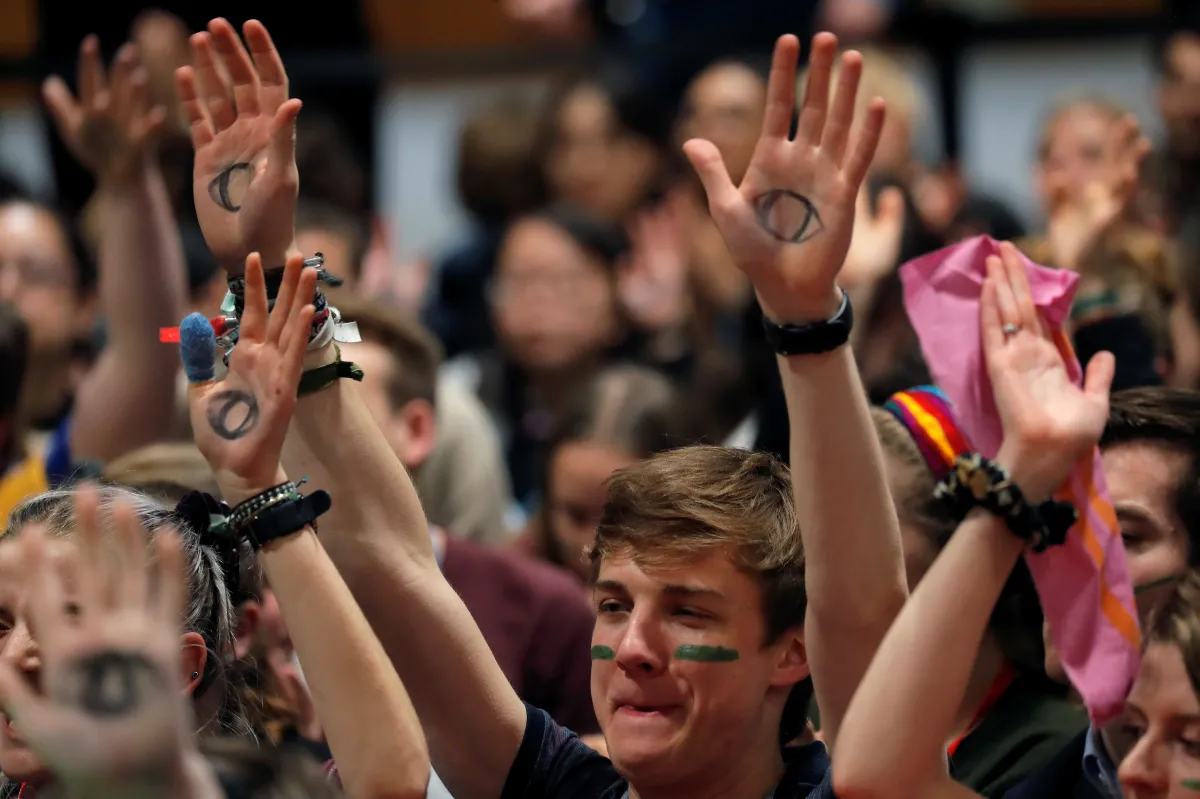 People with painted markings on their hands and faces raise their arms in a crowd