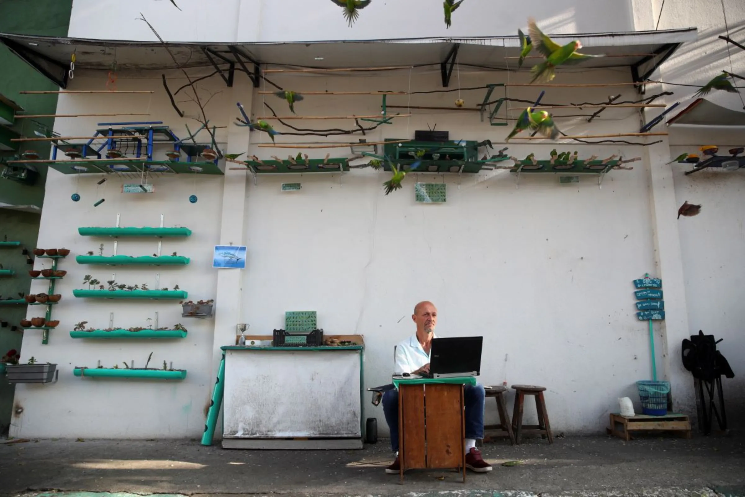A man looks on while sitting on the sidewalk with his computer as birds fly near him in Sao Paulo, Brazil June 30, 2022