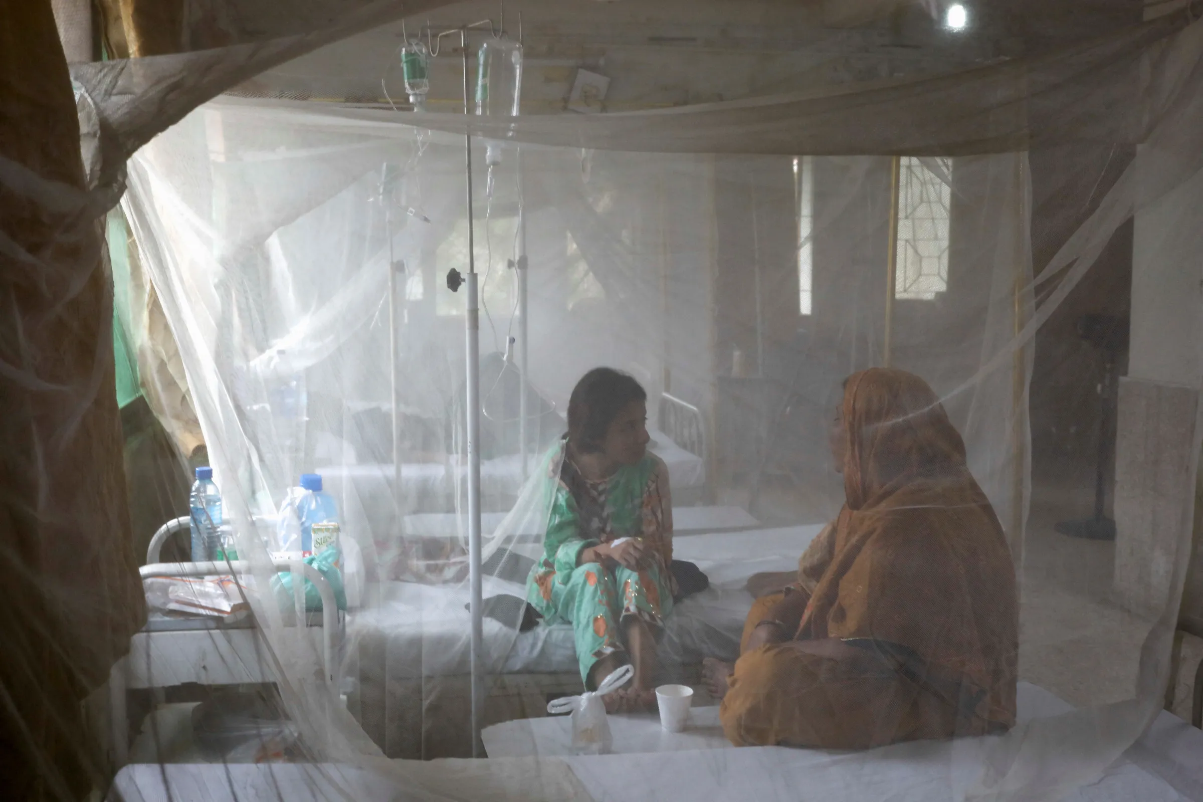 A patient suffering from dengue fever chats with a woman while sitting under a mosquito net inside a dengue and malaria ward at the Sindh Government Services Hospital in Karachi, Pakistan September 21, 2022