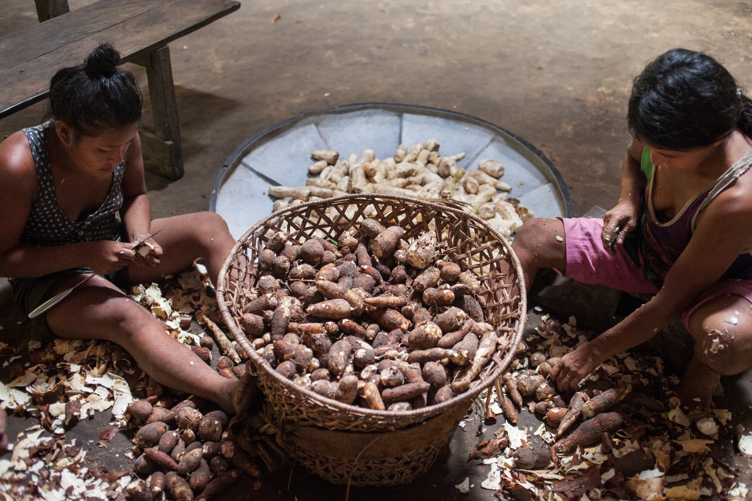 Two women sit around a basket of root vegetables