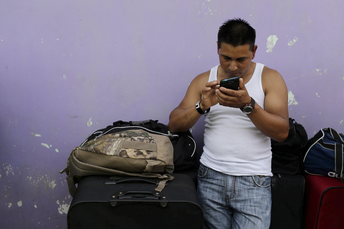 A man checks his phone as he leans against a pile of bags in front of a purple wall