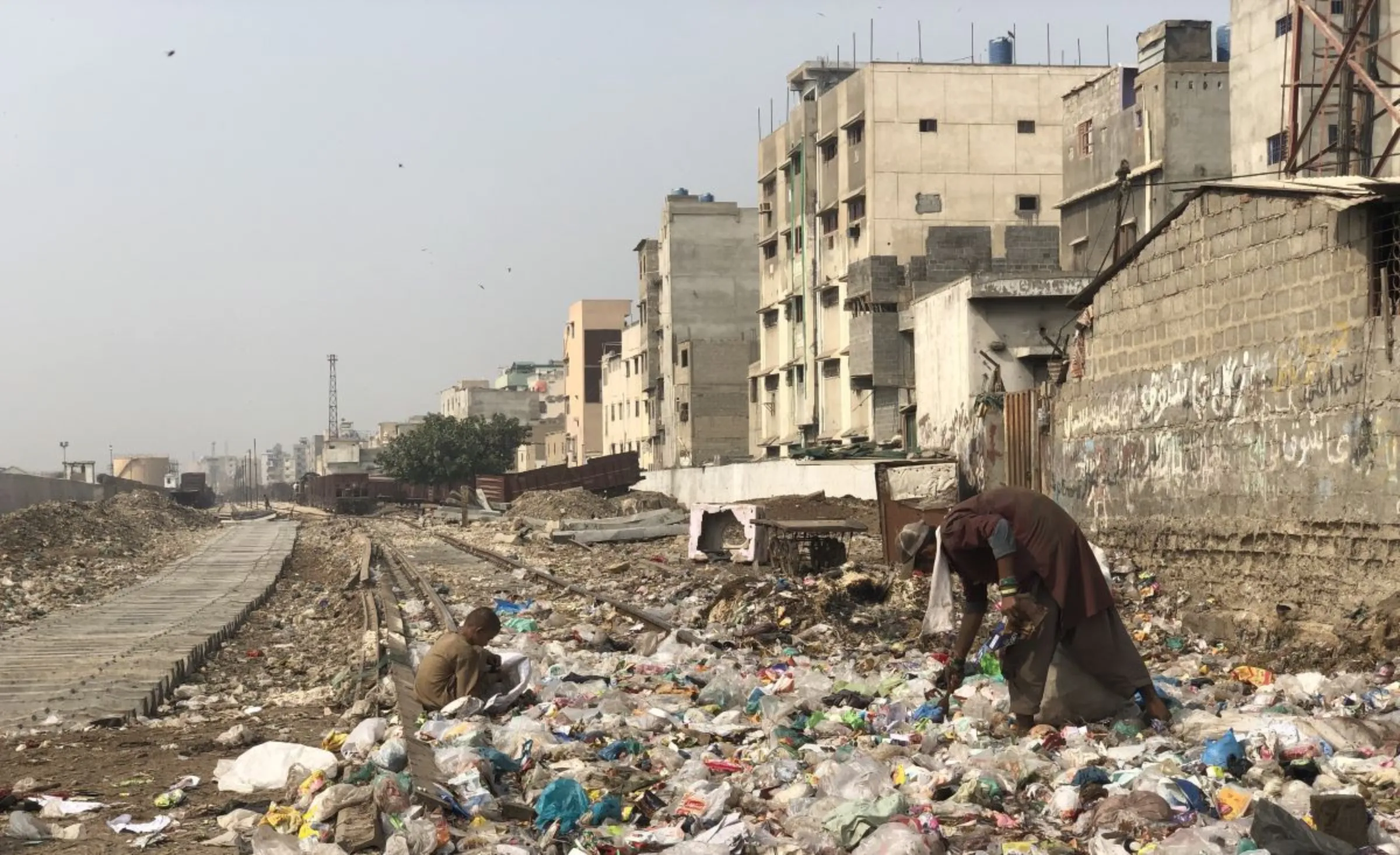 A child and a man collect garbage from railway tracks behind the informal settlement of Shireen Jinnah Colony in Karachi, Pakistan, November 9, 2023