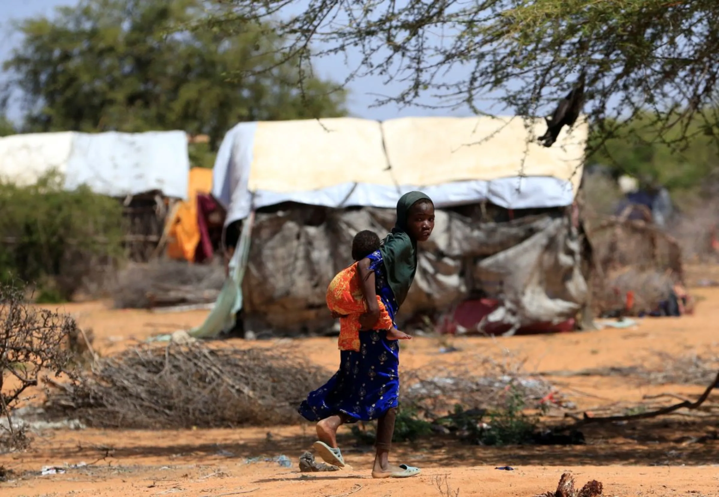A Somali refugee girl carries her sibling as they walk, fleeing drought, facing malnutrition and cholera, in their new arrivals area of the Hagadera refugee camp in Dadaab,  near the Kenya-Somalia border, in Garissa County, Kenya, January 17, 2023