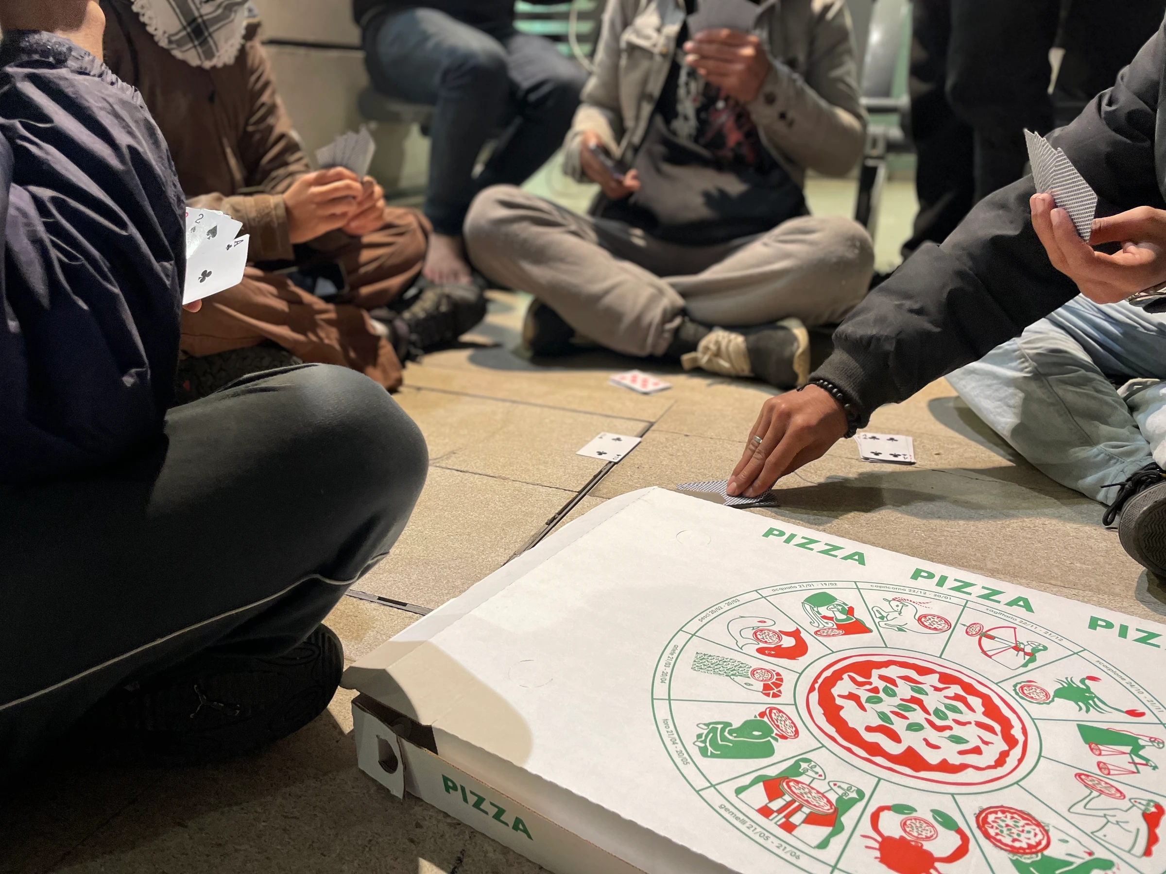 A group of Afghan teenagers and men play cards in Trieste Centrale railway station while waiting for a train to Venice, in Trieste, Italy. November 14, 2024. Thomson Reuters Foundation/Beatrice Tridimas