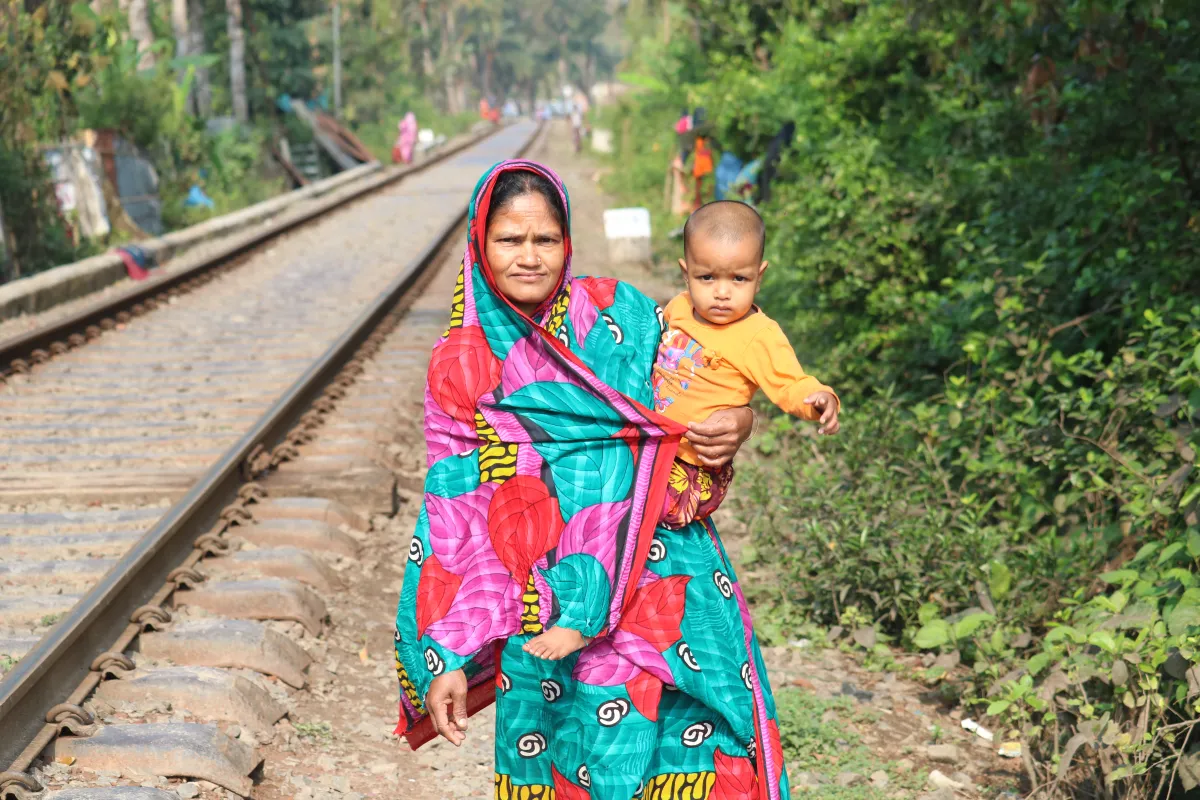A woman stands holding a child next to a railway line