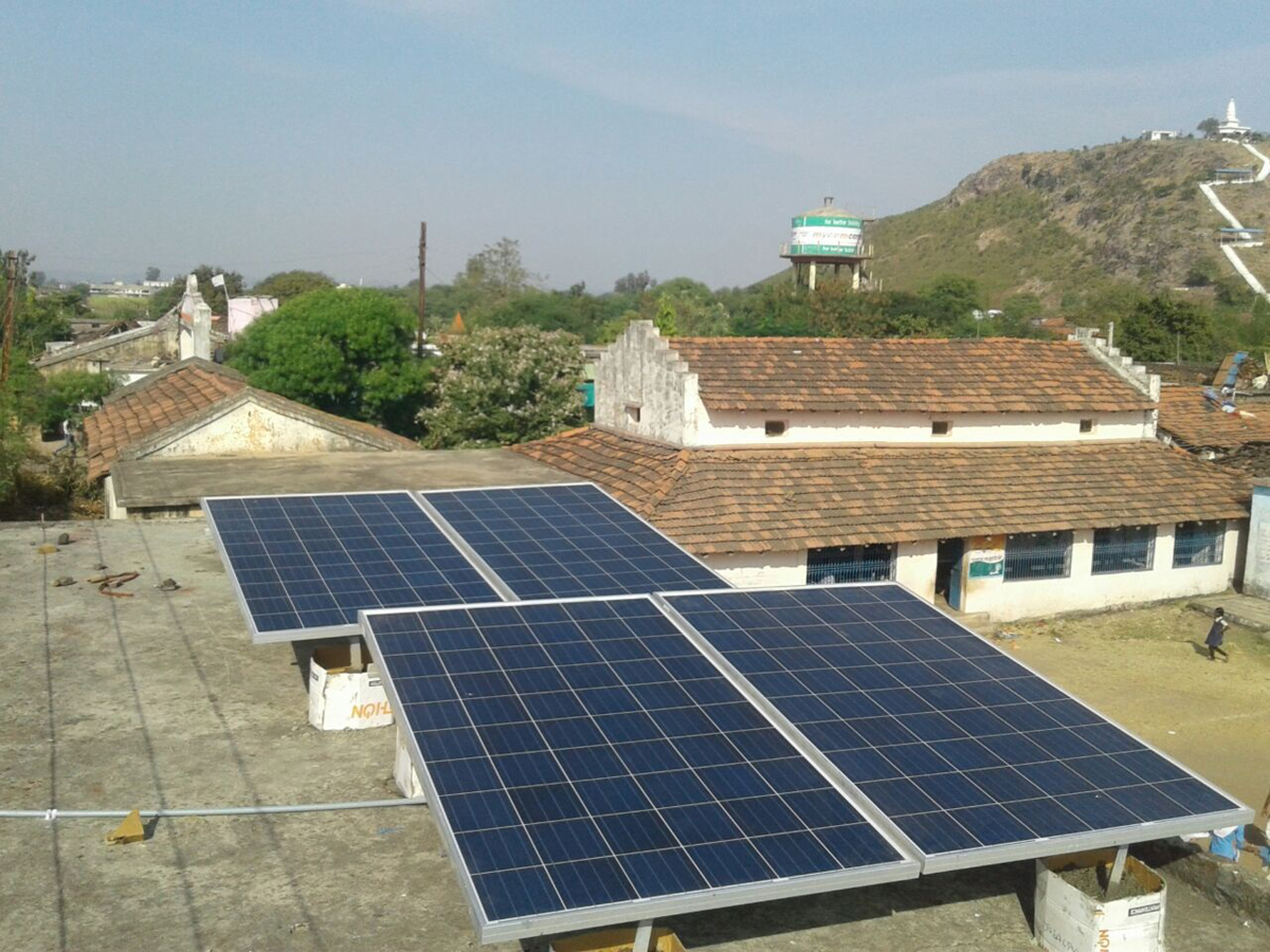 Solar panels are pictured on top of a roof in front of other buildings