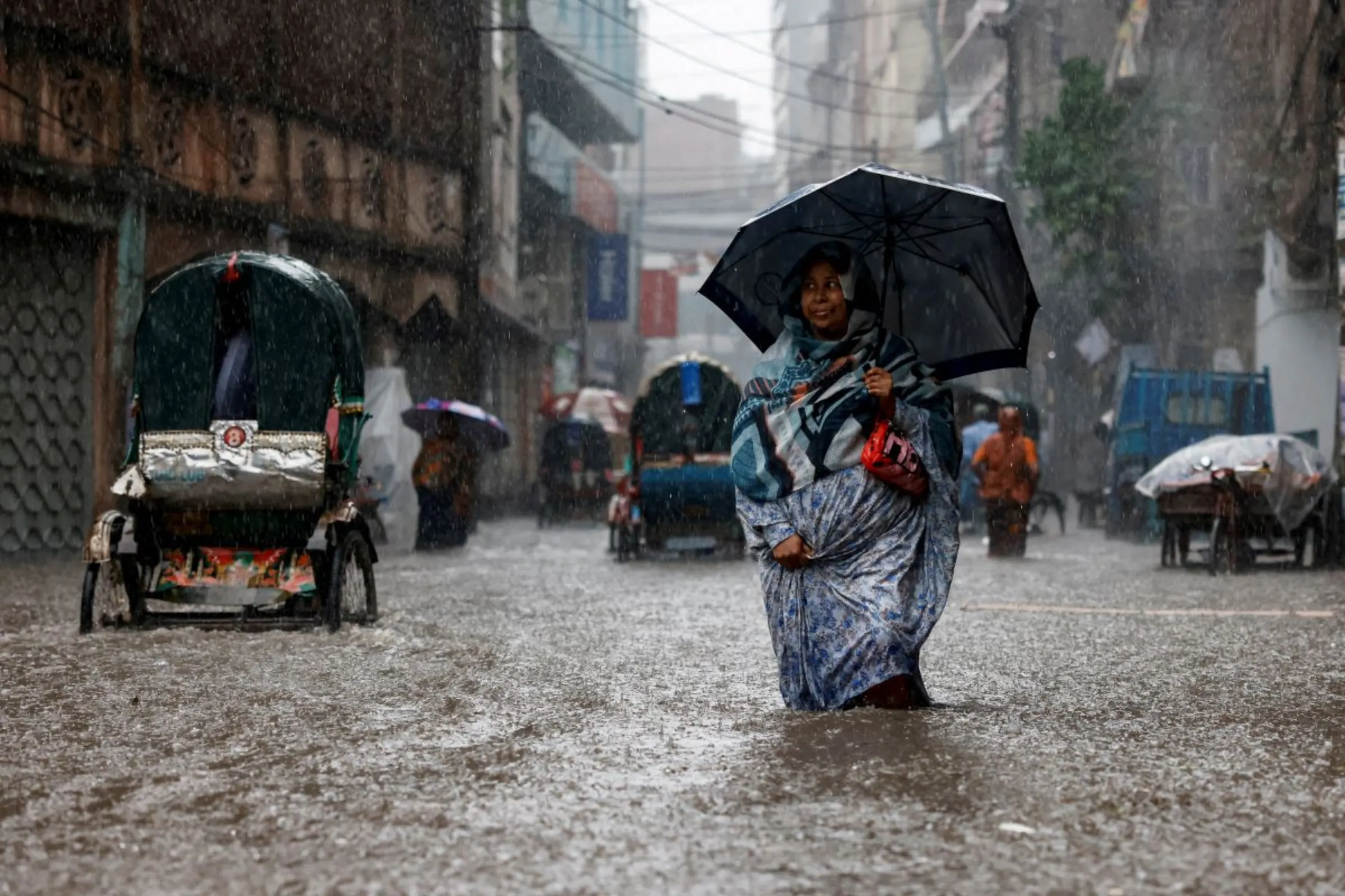 A woman holds an umbrella while walking along a flooded street during heavy rain in Dhaka, Bangladesh, June 12, 2023. REUTERS/Mohammad Ponir Hossain