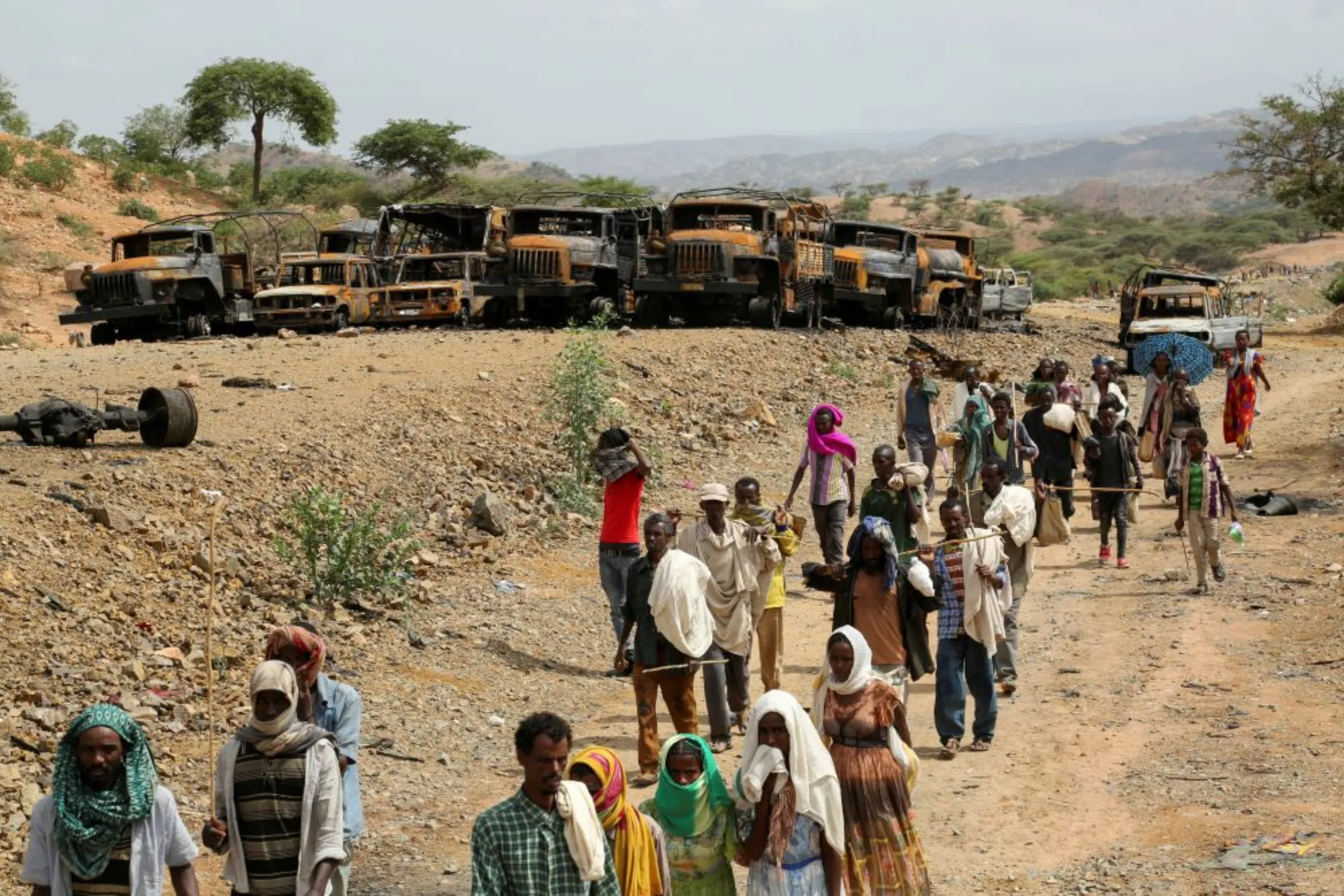 Villagers return from a market to Yechila town in south central Tigray walking past scores of burned vehicles, in Tigray, Ethiopia, July 10, 2021