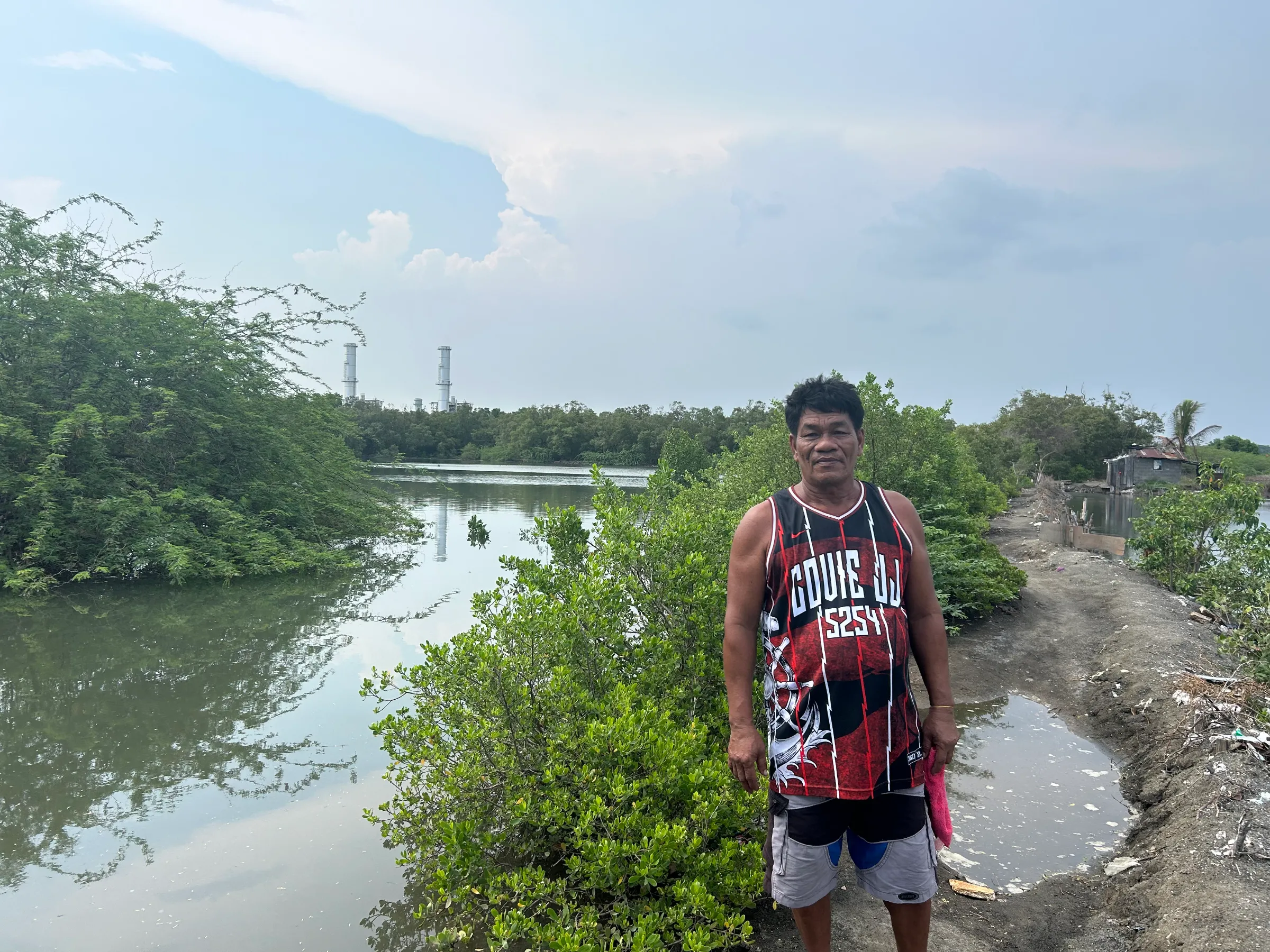 Joseph Vargas stands on the banks of a river where a power plant can be seen near their home in Santa Clara, Batangas, Philippines. June 12, 2024. Mariejo Ramos/Thomson Reuters Foundation