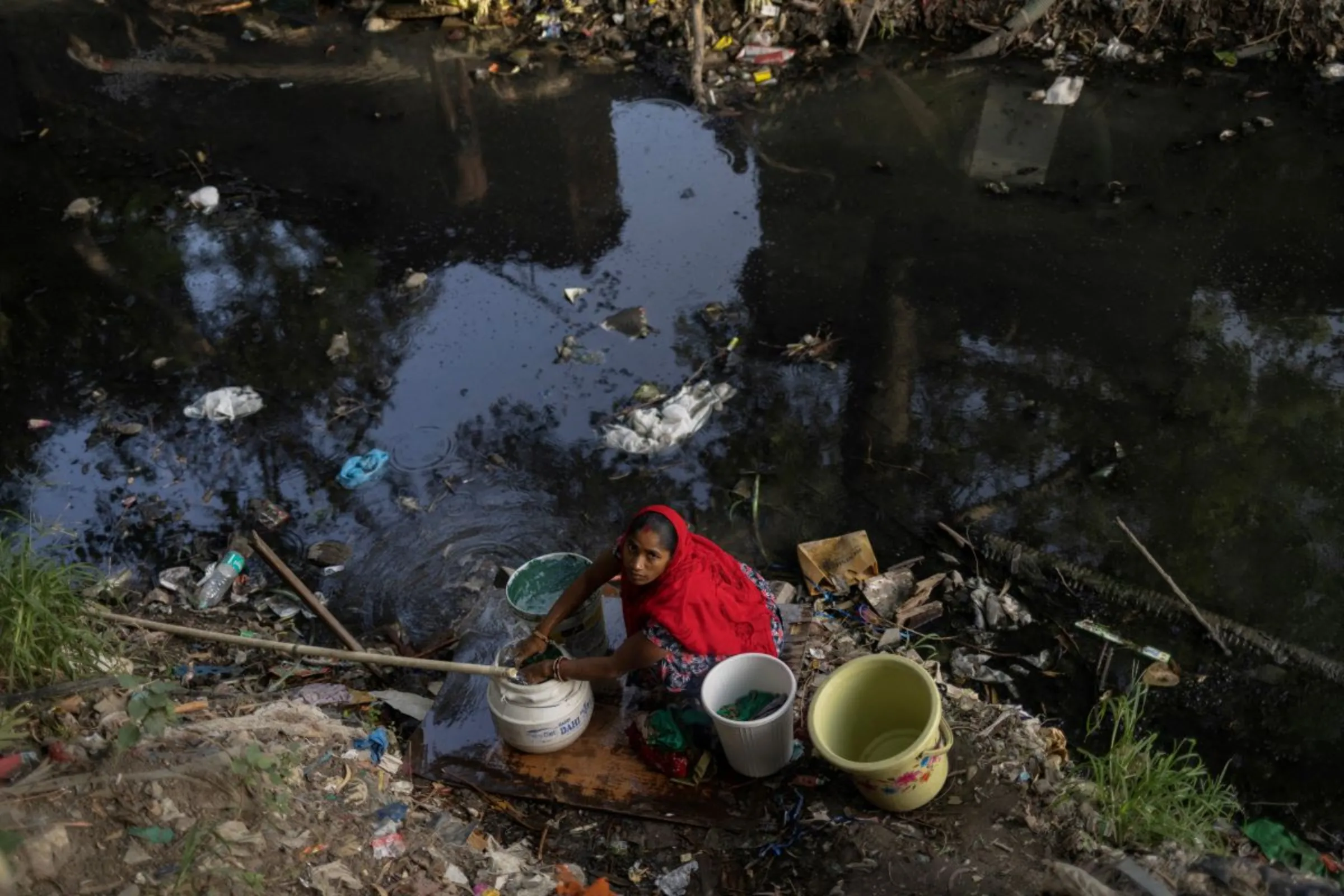 A woman fills drinking water in containers next to a drain behind the slum area before it was demolished by the authorities near the upcoming G20 Summit main venue in New Delhi, India, May 26, 2023. REUTERS/Adnan Abidi