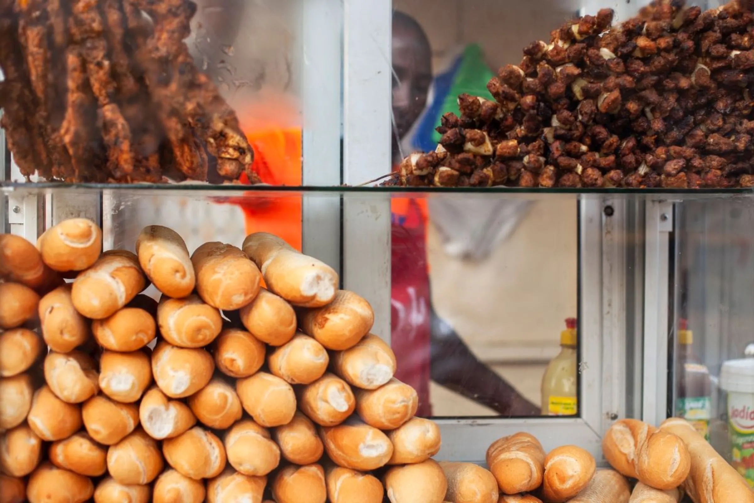 A food vendor stands behind his glass stall displaying meat and bread in Ouakam, Dakar, Senegal, January 26, 2022. Marta Moreiras for StreetNet/Handout via Thomson Reuters Foundation