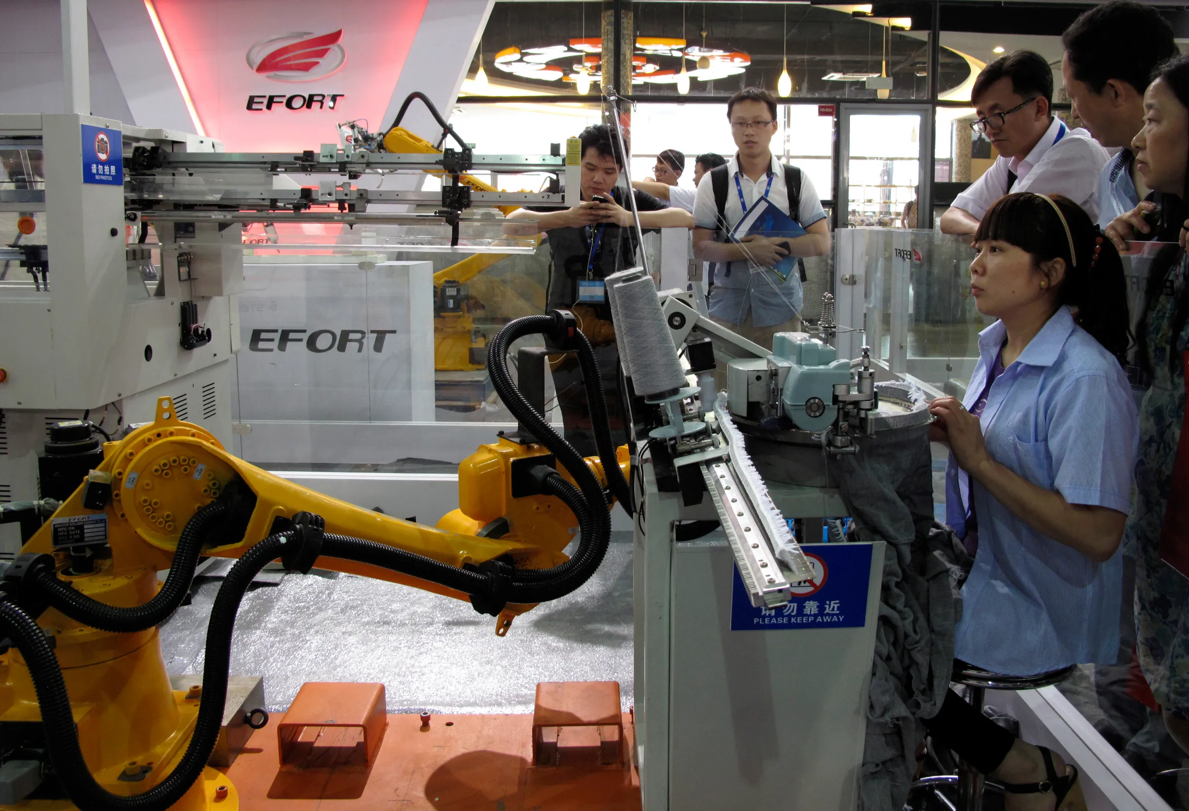 A woman (sitting) races with a textile robot (L) made by domestic manufacturer Anhui Efort at an expo in Shanghai July 10, 2014. REUTERS/Pete Sweeney