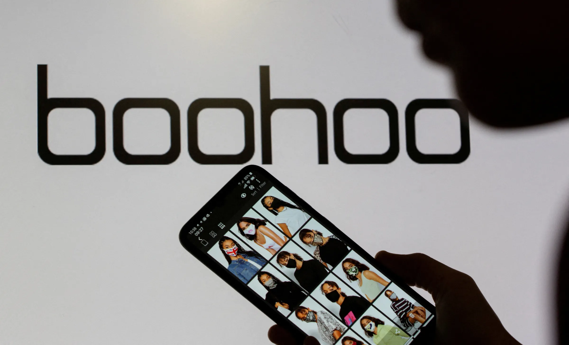 A woman poses with a smartphone showing the Boohoo app in front of the Boohoo logo on display in this illustration taken September 30, 2020. REUTERS/Dado Ruvic