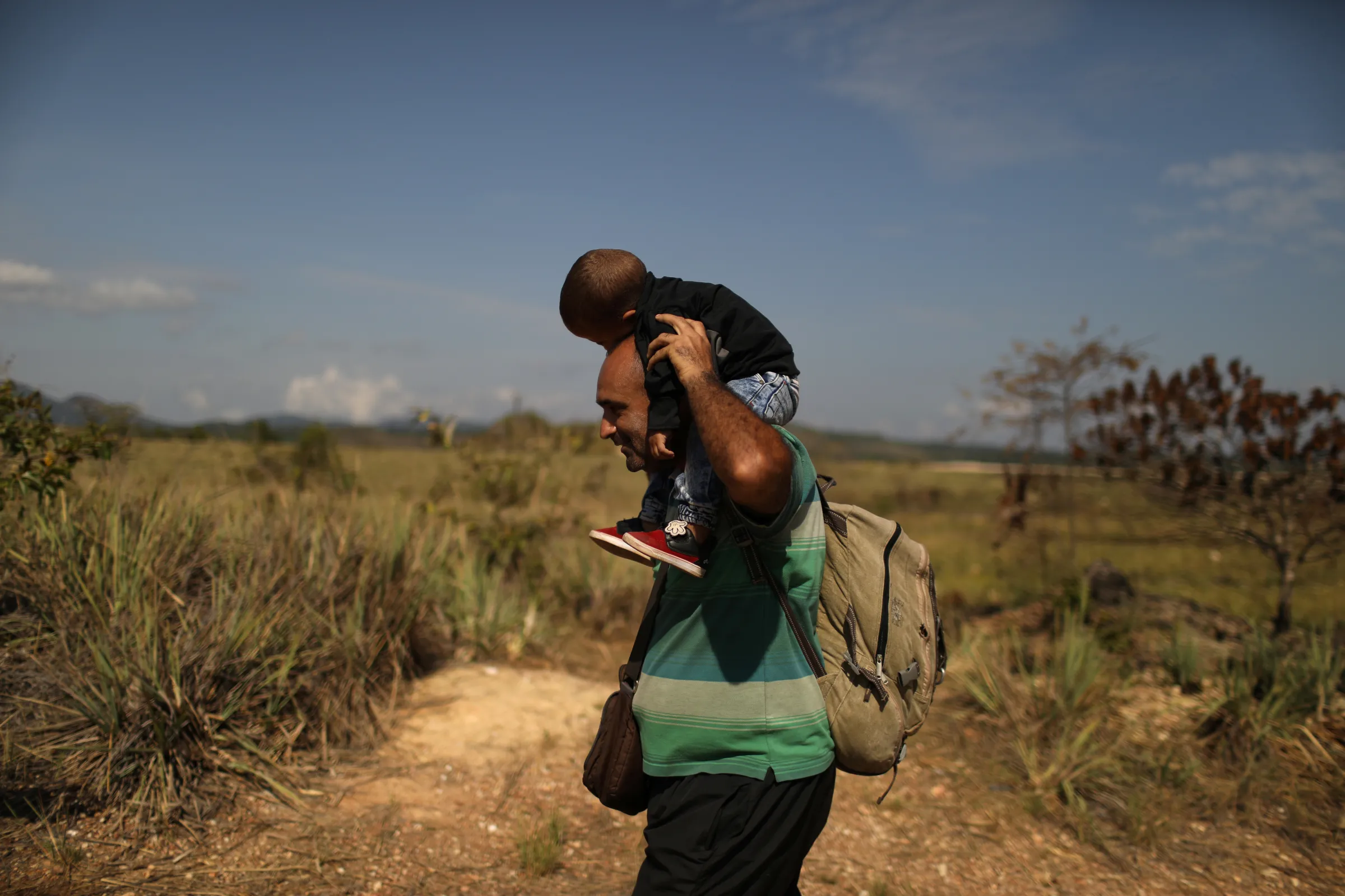 A Venezuelan migrant carrying a baby walks along a trail into Brazil