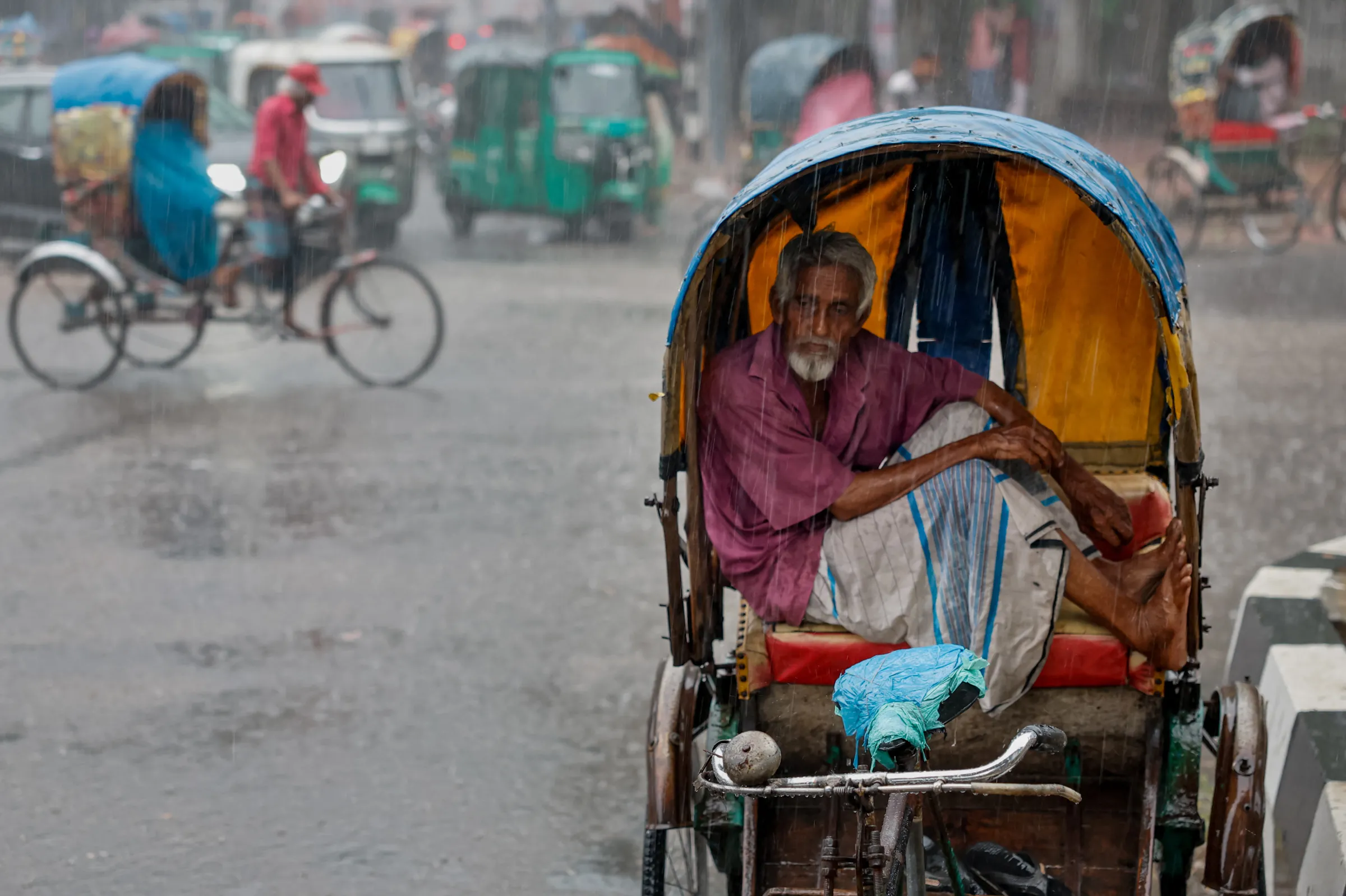 A rickshaw driver sits inside his rickshaw to take cover from rain during a downpour in Dhaka, Bangladesh, June 13, 2024. REUTERS/Mohammad Ponir Hossain