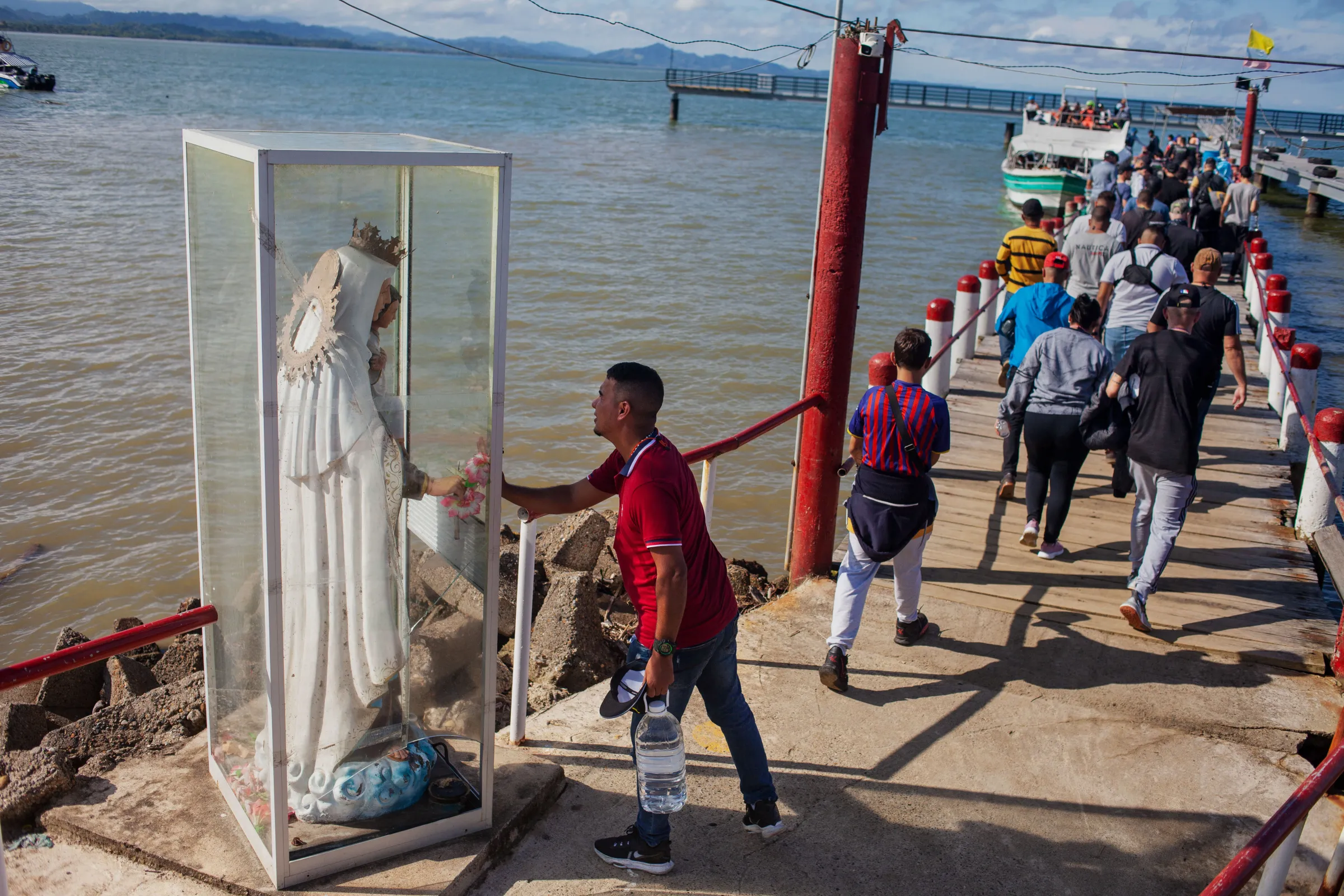Migrants from Venezuela, Haiti, and parts of Africa and Asia walk along the pier in Necoclí to board a tourist boat to cross the Gulf of Urabá to reach Capurganá from where the jungle trek begins. Necoclí, Colombia, July 26, 2022. Thomson Reuters Foundation/Fabio Cuttica
