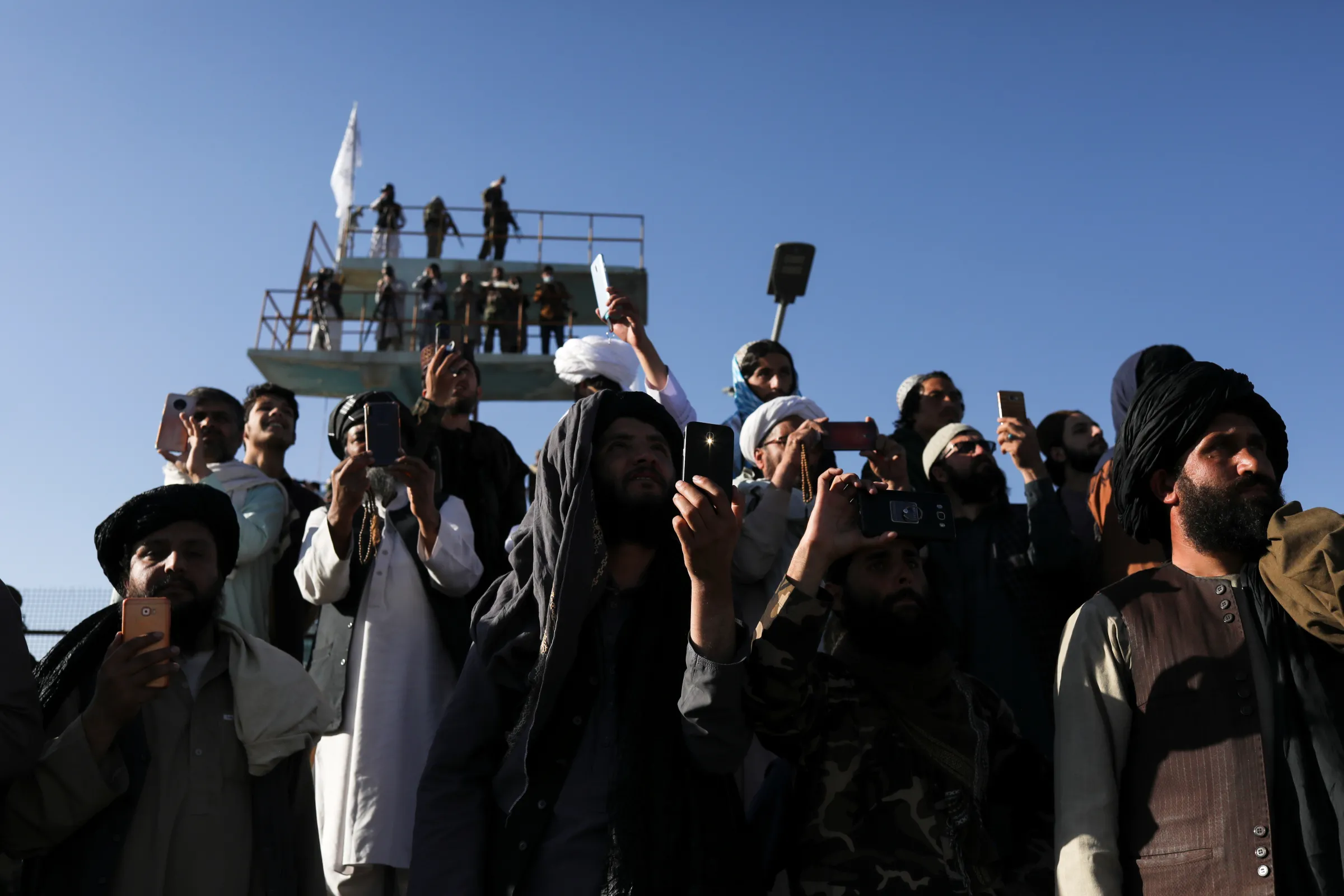 Taliban members take pictures with their mobile phones during the Taliban flag-raising ceremony in Kabul