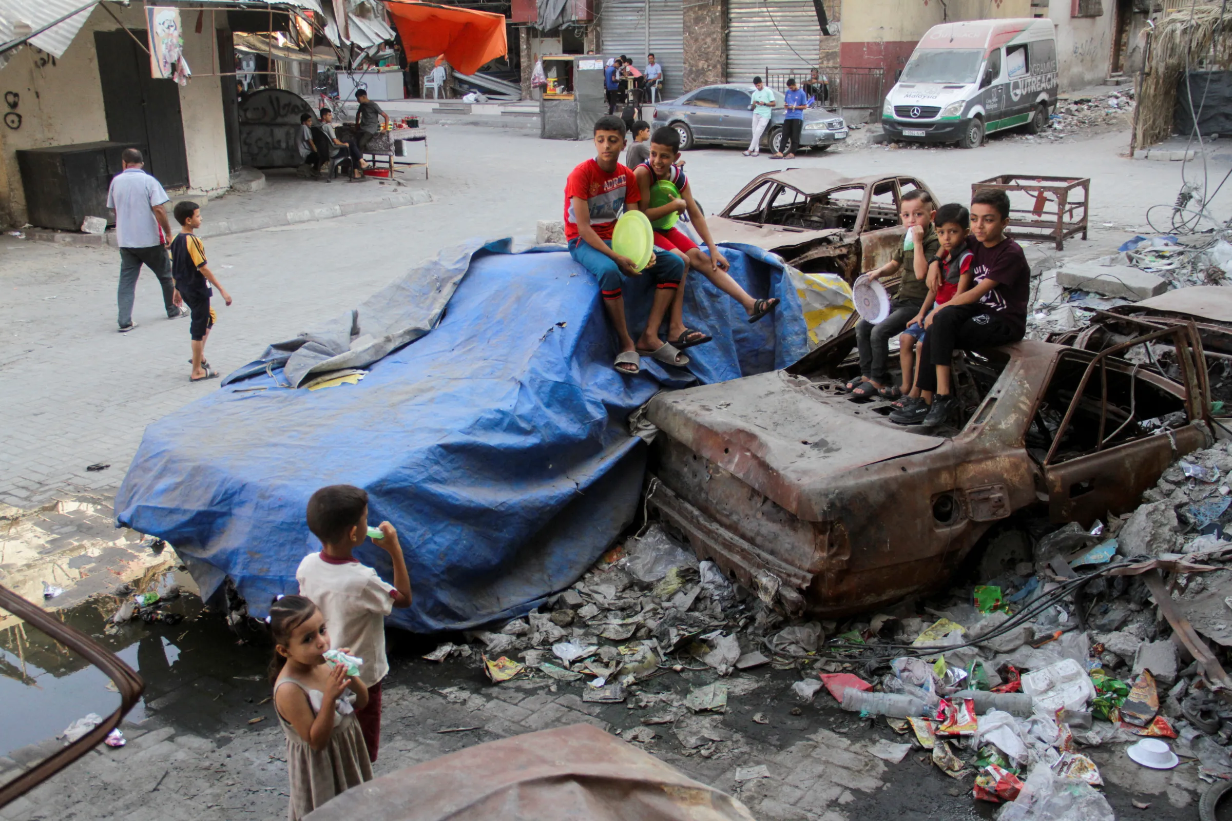 Children sit on damaged cars, as Palestinians wait to receive food cooked by a charity kitchen, amid a hunger crisis as conflict between Israel and Hamas continues, in the northern Gaza Strip August 14, 2024. REUTERS/Mahmoud Issa