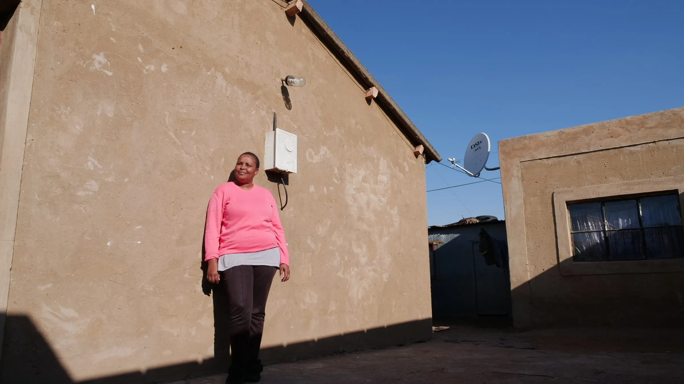 Ntombikayise Setyila stand outside her home where he rechargeable light has been installed on her wall
