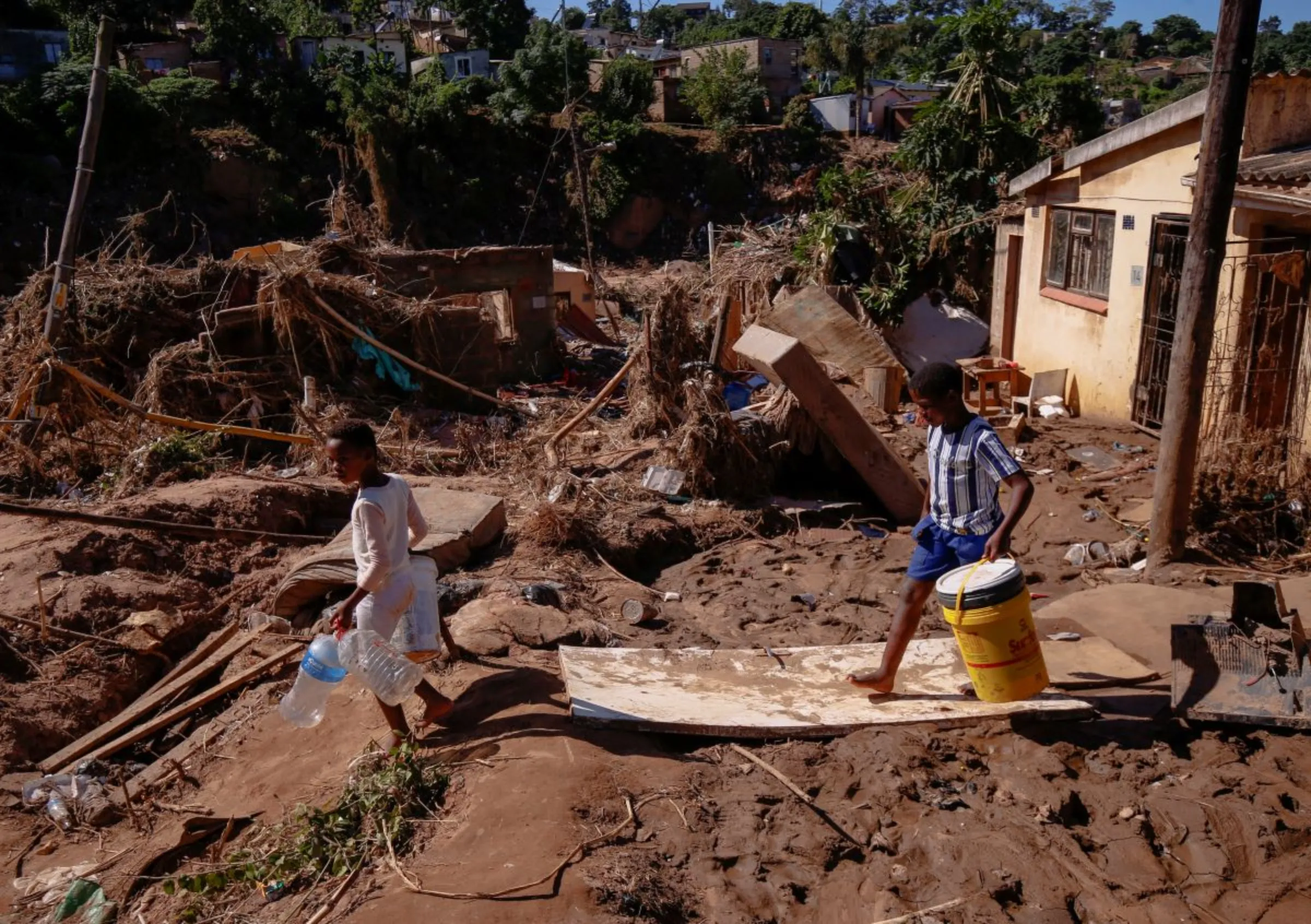 Children walk next to damaged houses to collect water after heavy rains caused flooding in Ntuzuma near Durban, South Africa, April 20, 2022. REUTERS/Rogan Ward