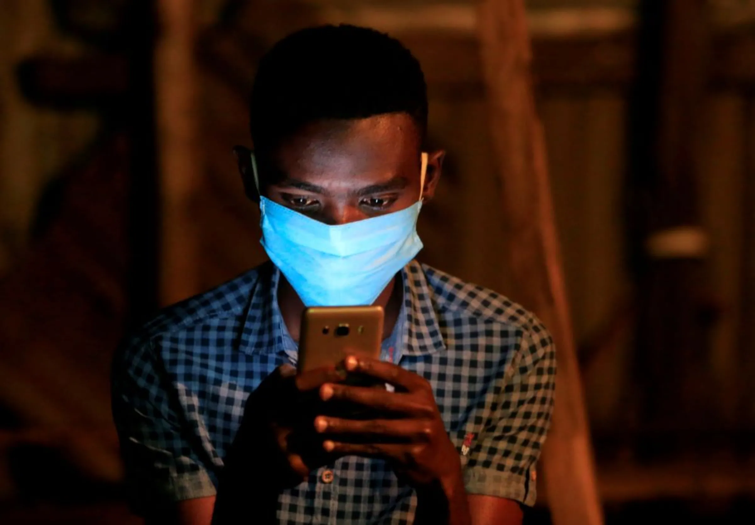 A soccer fan uses his mobile phone for betting during a television broadcast at a soccer theatre called the San Siro Stadium as the English Premier League season resumes after a three-month stoppage due to the coronavirus disease (COVID-19) spread, in Kibera district of Nairobi, Kenya June 17, 2020