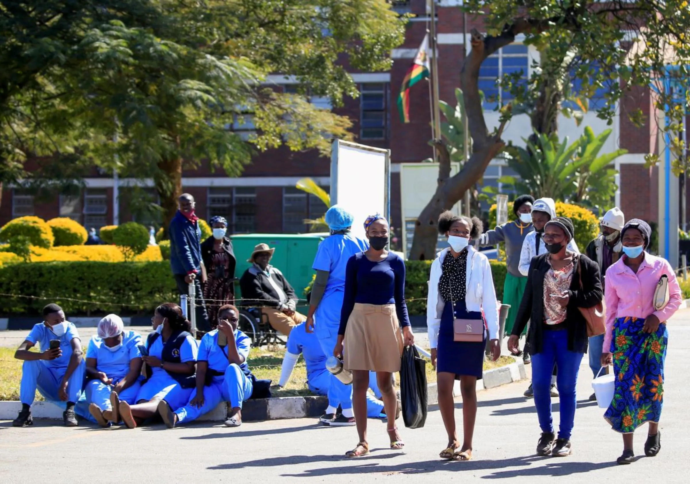 Poeple walk past Zimbabwean medical workers as they sit outside Sally Mugabe Hospital during a strike by state doctors and nurses to press for higher pay, in Harare, Zimbabwe, June 20, 2022. REUTERS/Philimon Bulawayo
