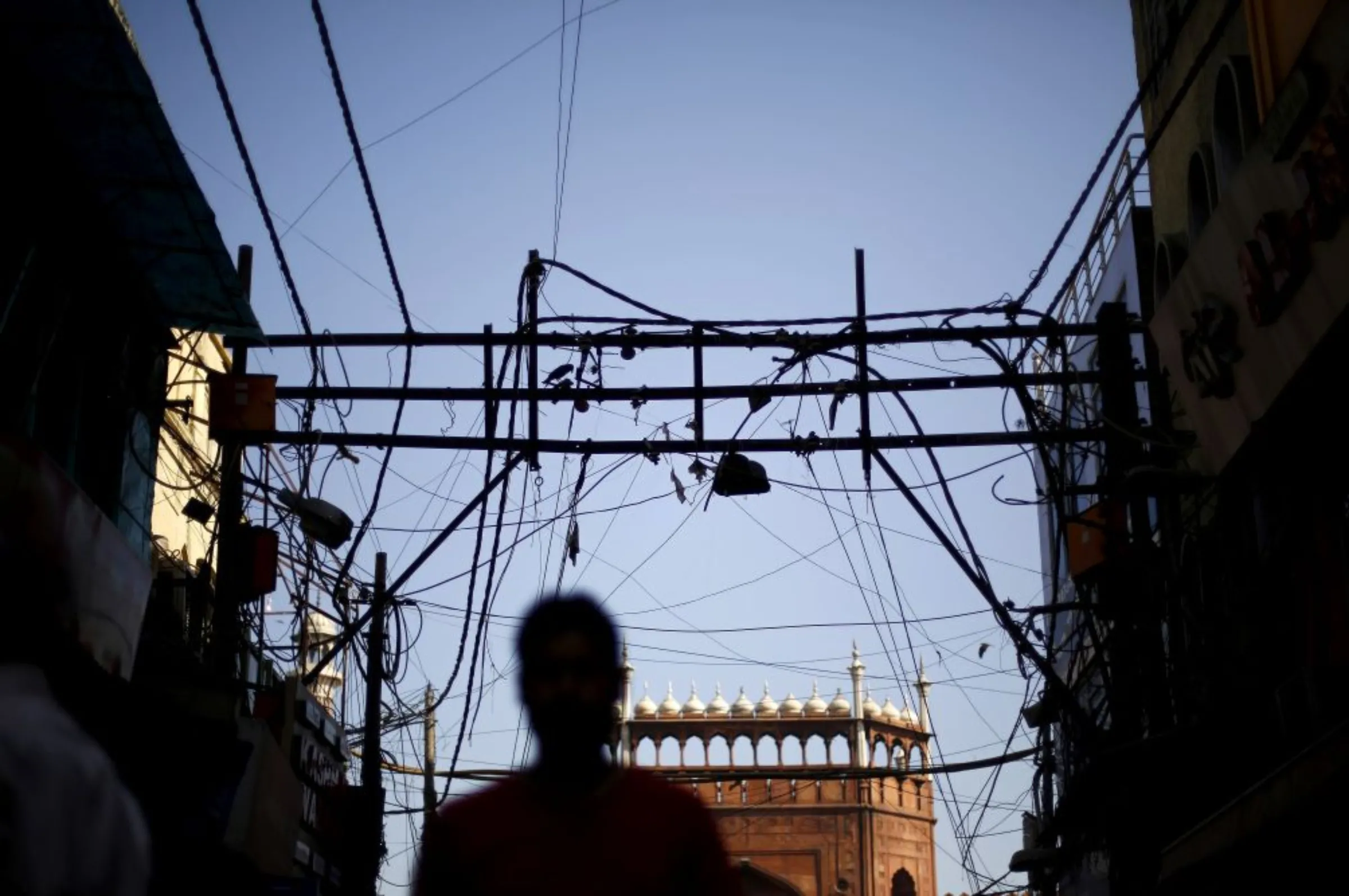 A man is silhouetted against the backdrop of Jama Masjid (Grand Mosque) as overhead power cables are seen in the old quarters of Delhi, India, September 10, 2015