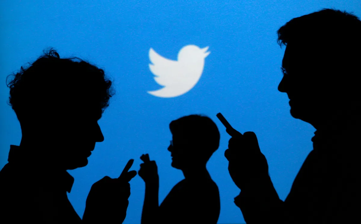 People holding mobile phones are silhouetted against a backdrop projected with the Twitter logo in this illustration picture taken in Warsaw September 27, 2013