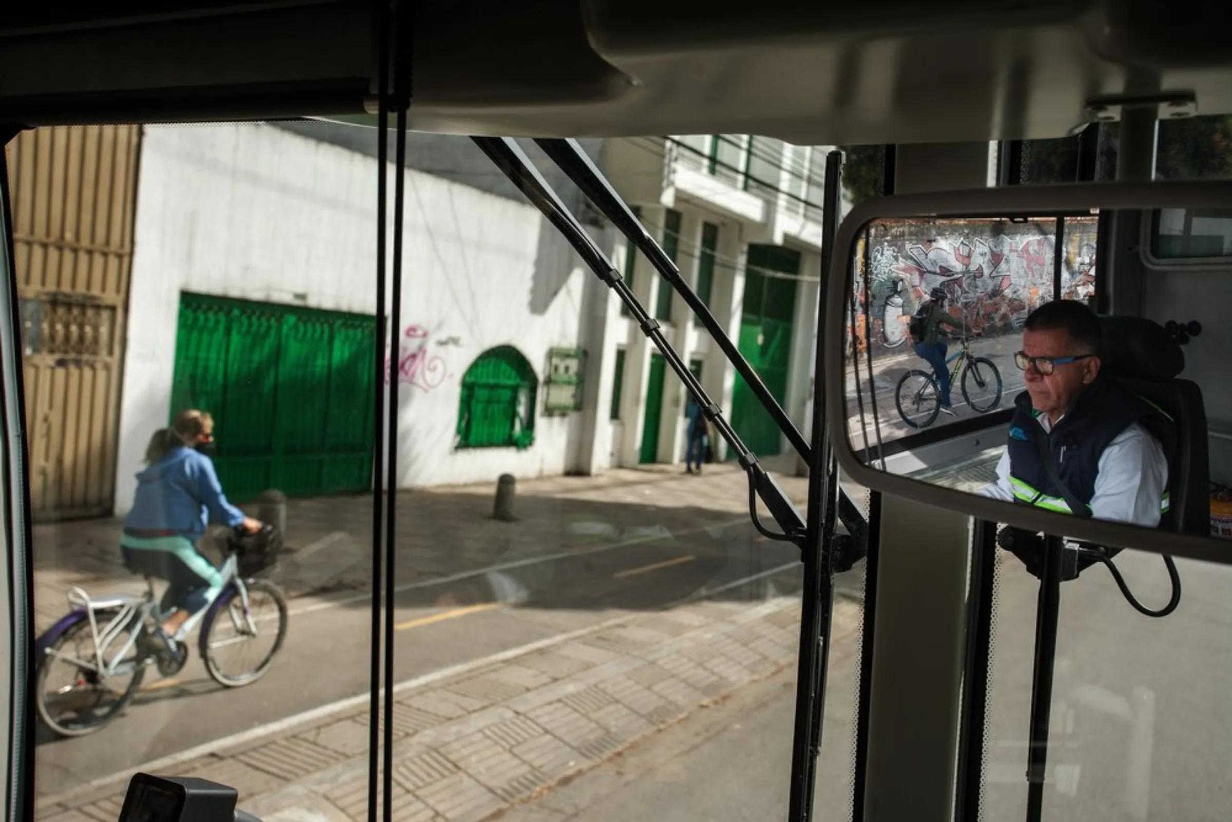 As a cyclist passes, driver Cesar Cantillo operates an electric bus on the road in Bogota, Colombia, April 21, 2021