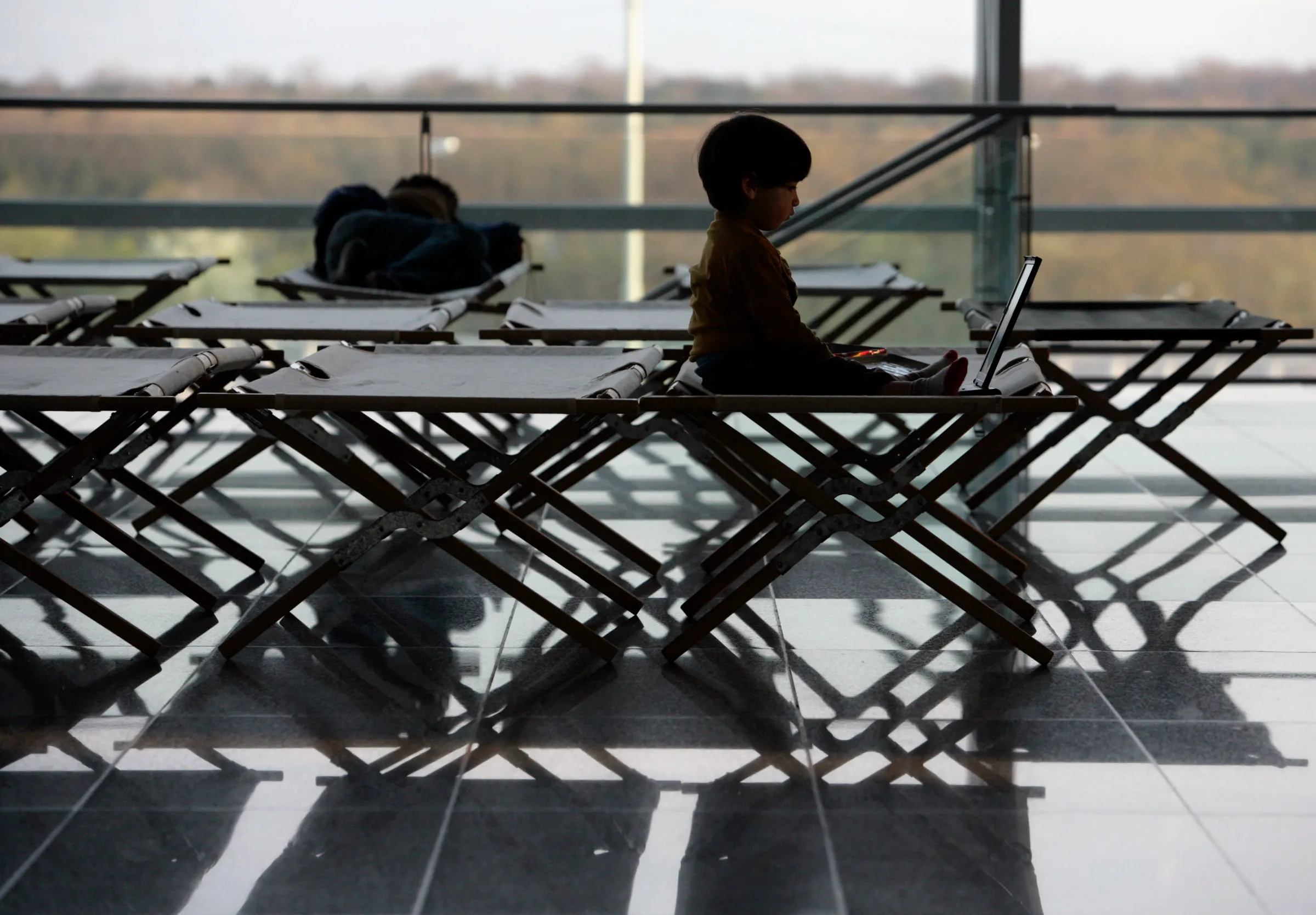 A child using a laptop sits on a camp bed