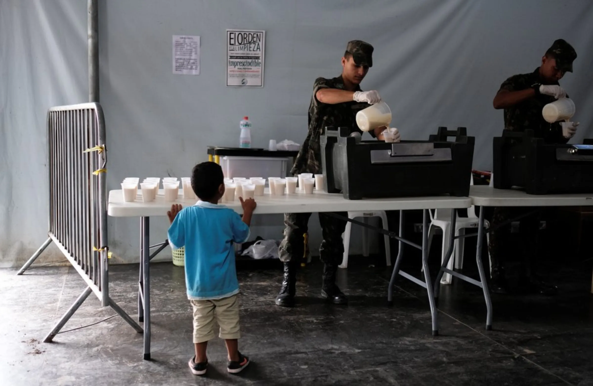 Military officers pour coffee with milk into plastic cups as a Venezuelan boy looks at them at the Pacaraima border control, Roraima state, Brazil August 8, 2018