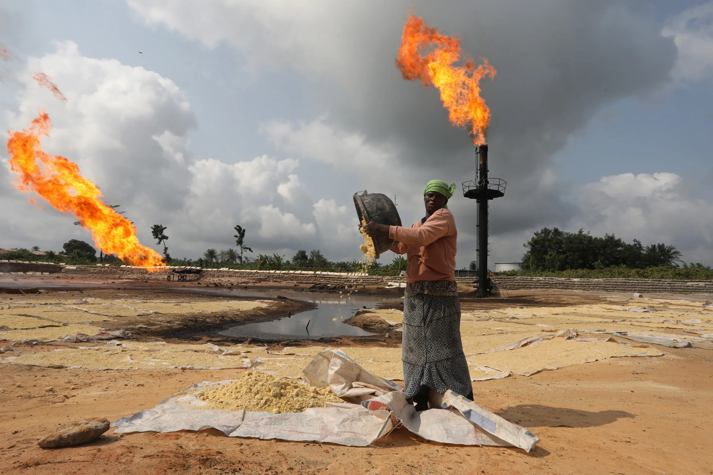 A woman empties a plastic bowl filled with tapioca on sewn sacks laid on the ground close to a gas flaring furnace in Ughelli, Delta State, Nigeria September 17, 2020. REUTERS/Afolabi Sotunde