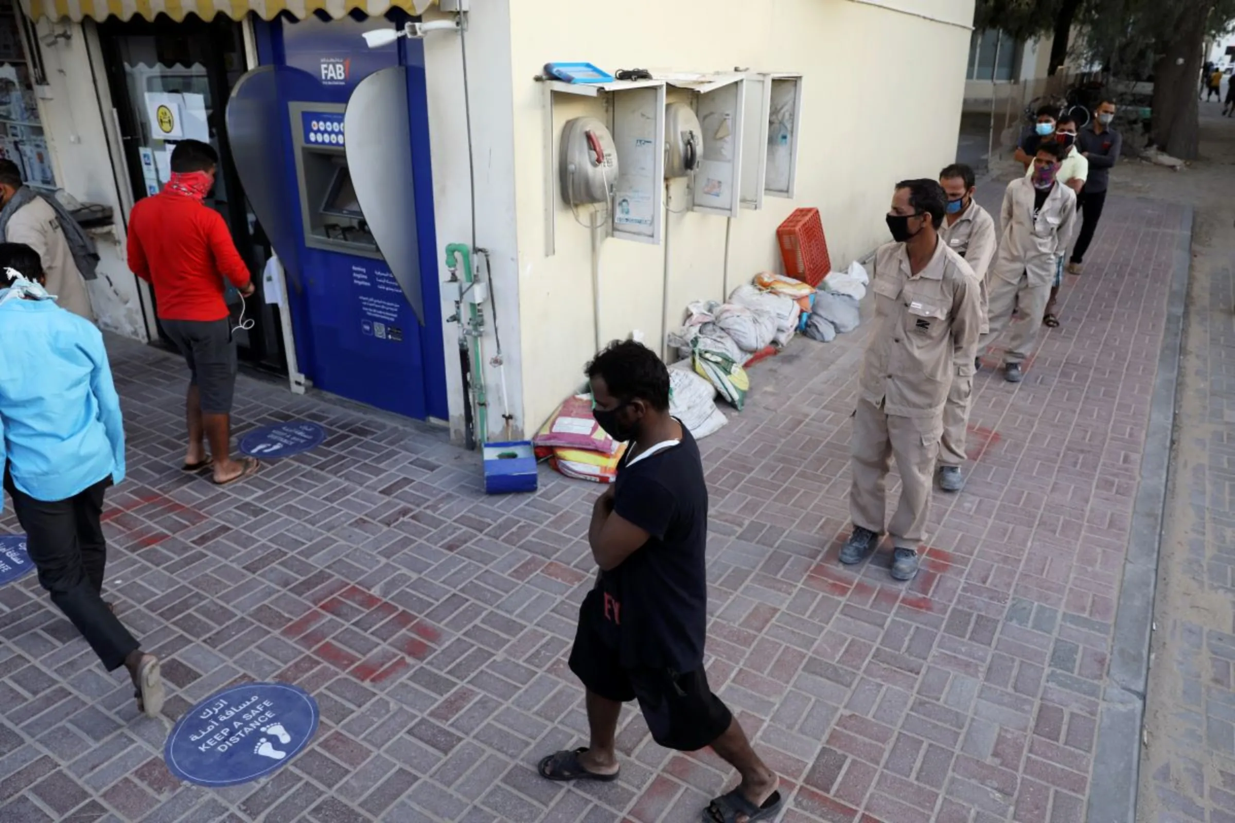 Foreign workers wearing protective face masks queue to use an ATM, in the Al Quoz industrial district of Dubai, United Arab Emirates, April 14, 2020