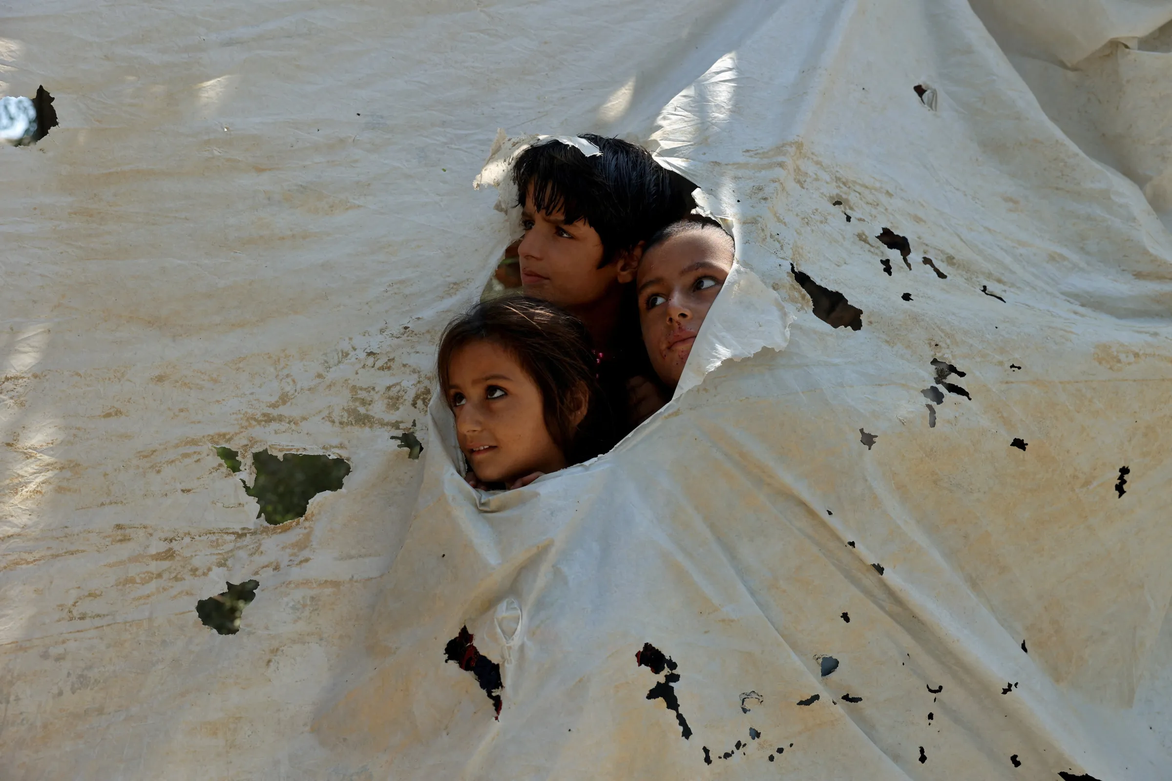 Children look out from a torn tent at a repatriation centre in Nowshera, Pakistan, as their families prepare to return to Afghanistan after Pakistan started to deport documented Afghan refugees, August 27, 2025. REUTERS/Fayaz Aziz