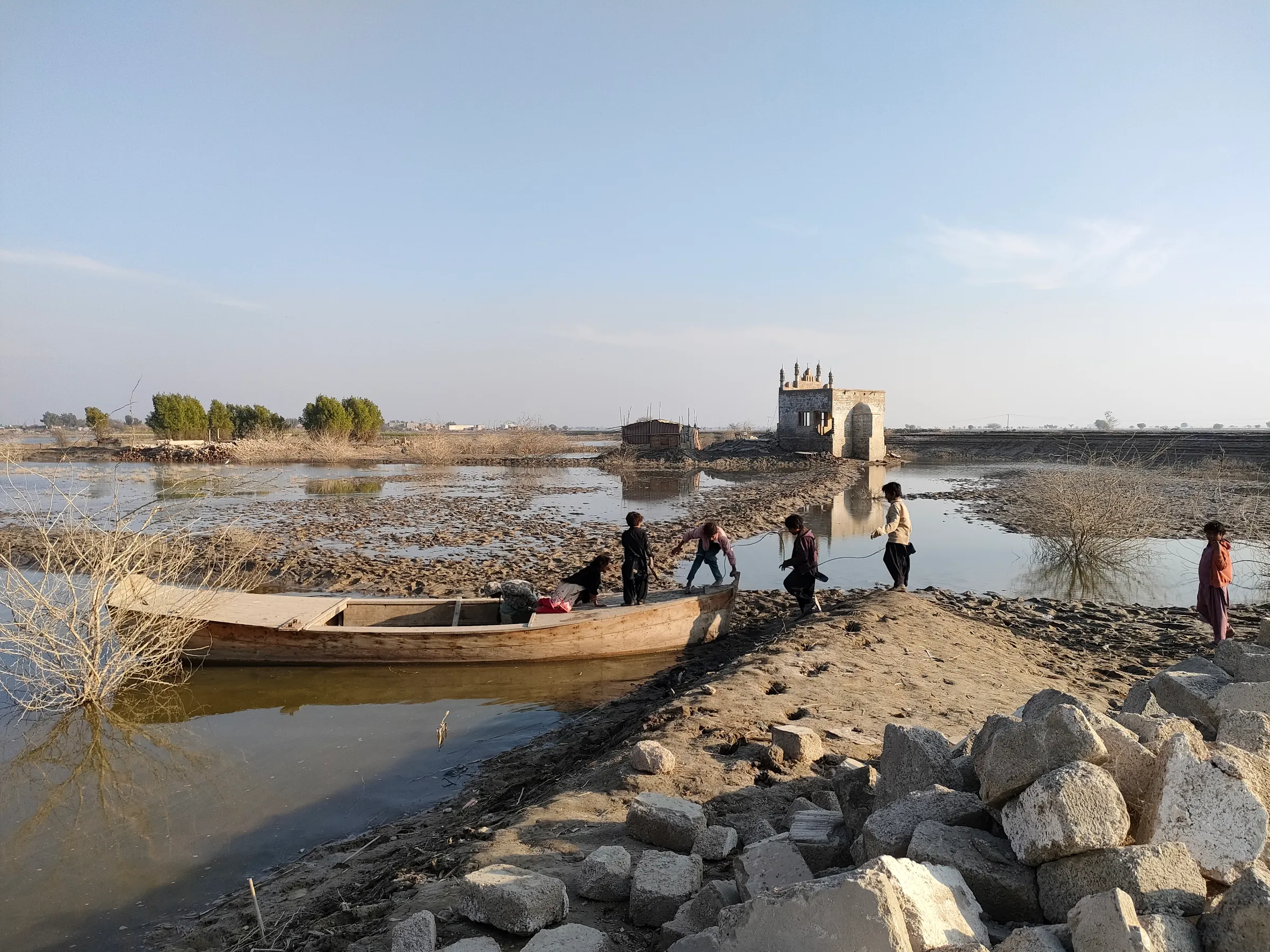 Children playing on a boat in putrid floodwater at village Goth Pechaho, Pakistan, January 17, 2023. Thomson Reuters Foundation/Waqar Mustafa