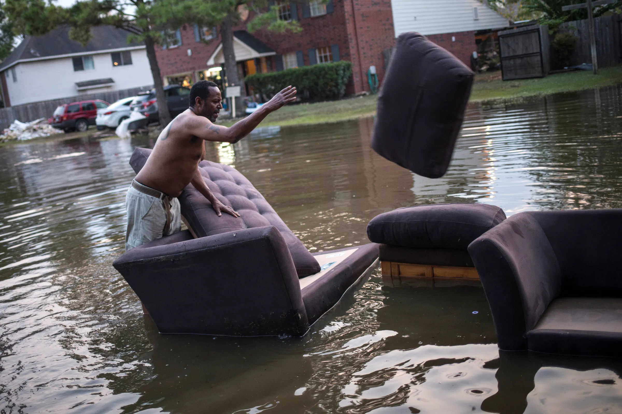A man throws sofa cushions in a flooded  street