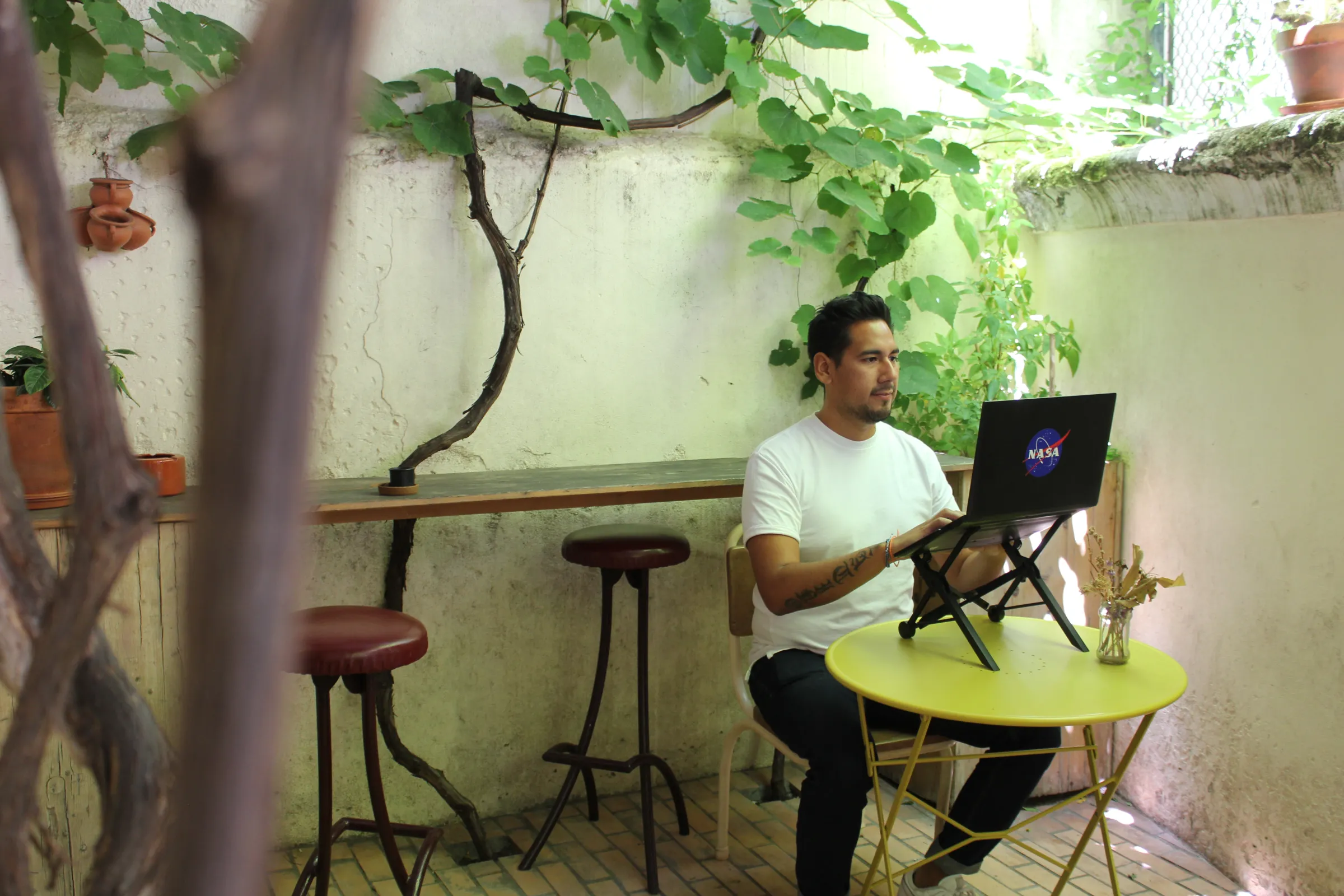 A man works on his laptop while sat in the patio of a cafe