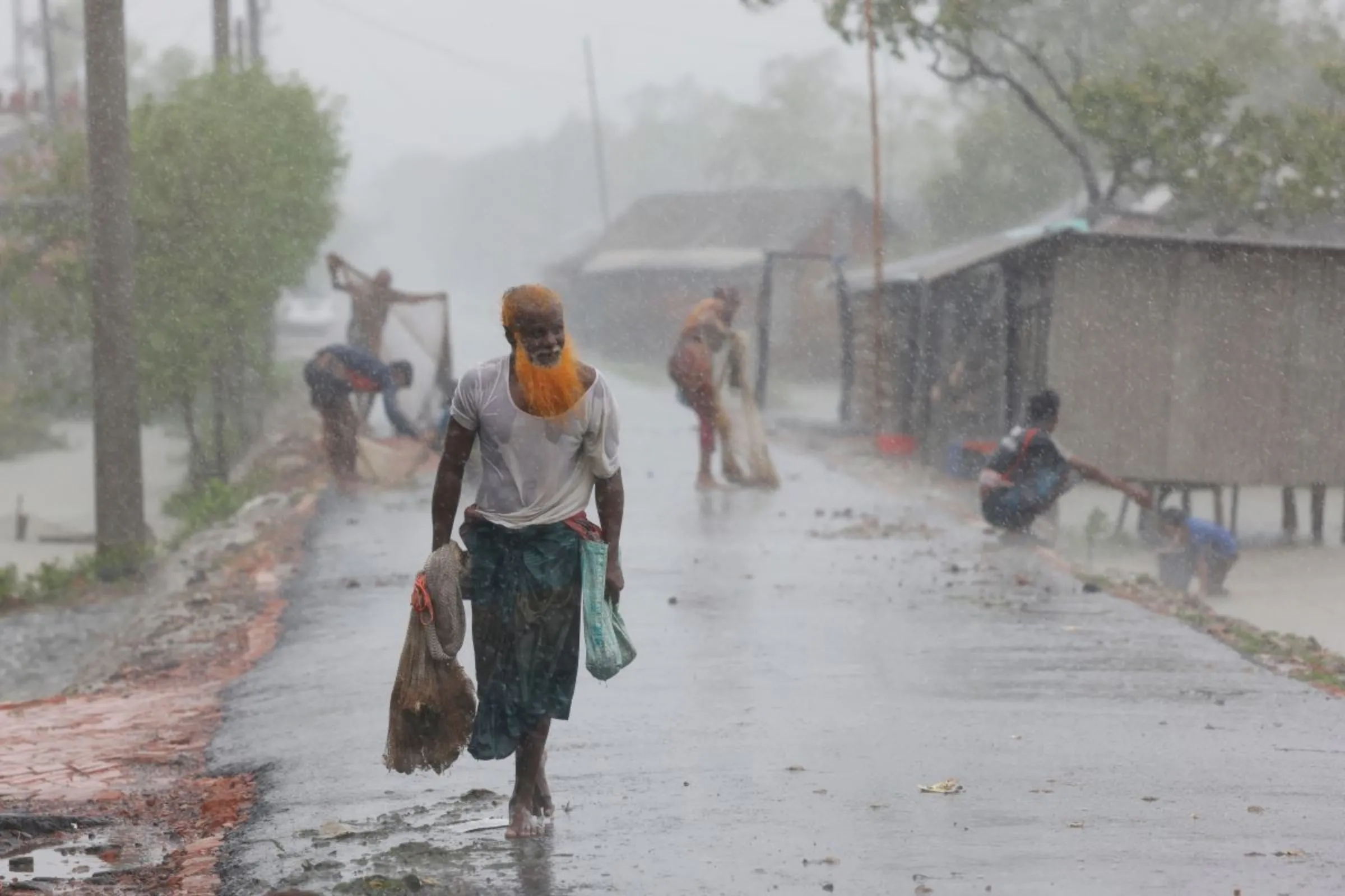 A man walks on the road with a net as people fish at the shrimp and crab farms that are flooded due to Cyclone Remal in Bangladesh, May 27, 2024. REUTERS/Mohammad Ponir Hossain