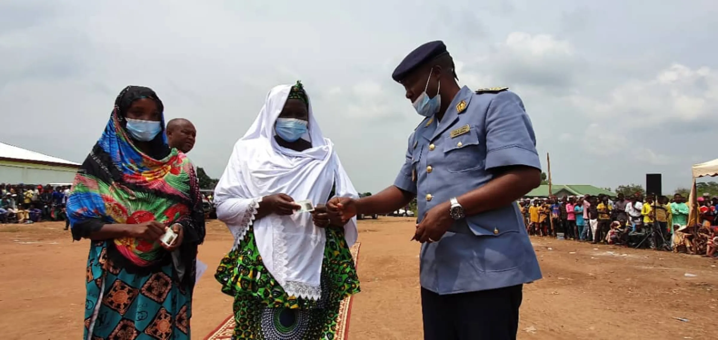 An official dressed in uniform hands out an ID card to a refugee standing with her friend in a camp in Cameroon