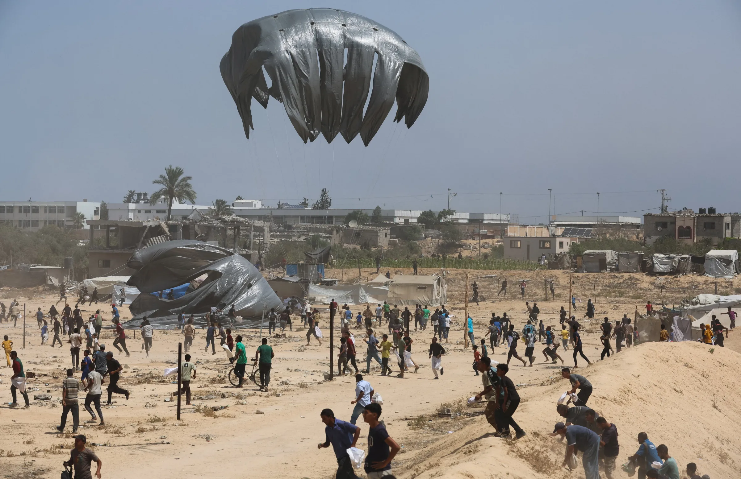 Palestinians run towards airdropped aid packages, in Deir Al-Balah, in the central Gaza Strip August 19, 2025. REUTERS/Ramadan Abed