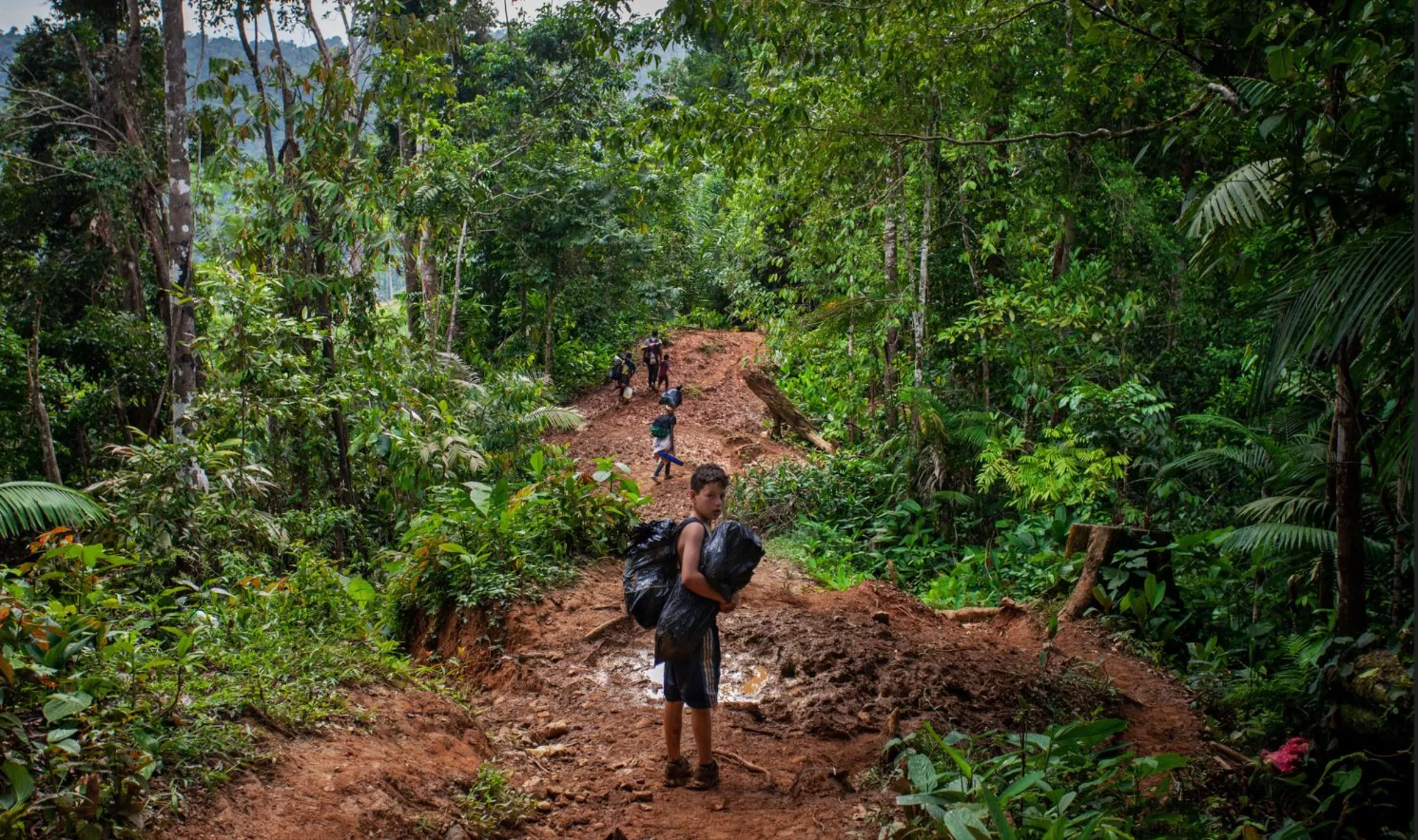 A Venezuelan boy, with his family behind him, walks through the Colombian jungle in the Darién Gap on day one of a five- to seven-day perilous and exhausting trek. Darién Gap, Colombia, July 27, 2022. Thomson Reuters Foundation/Fabio Cuttica