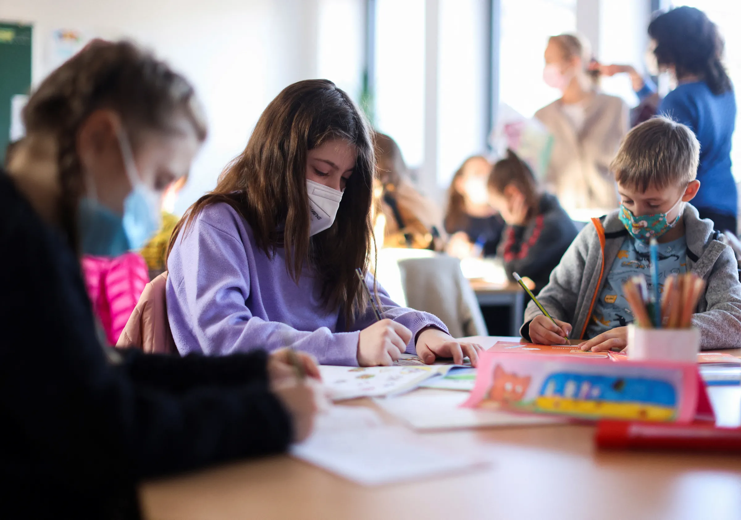 Children wearing facemasks sit working at a school table