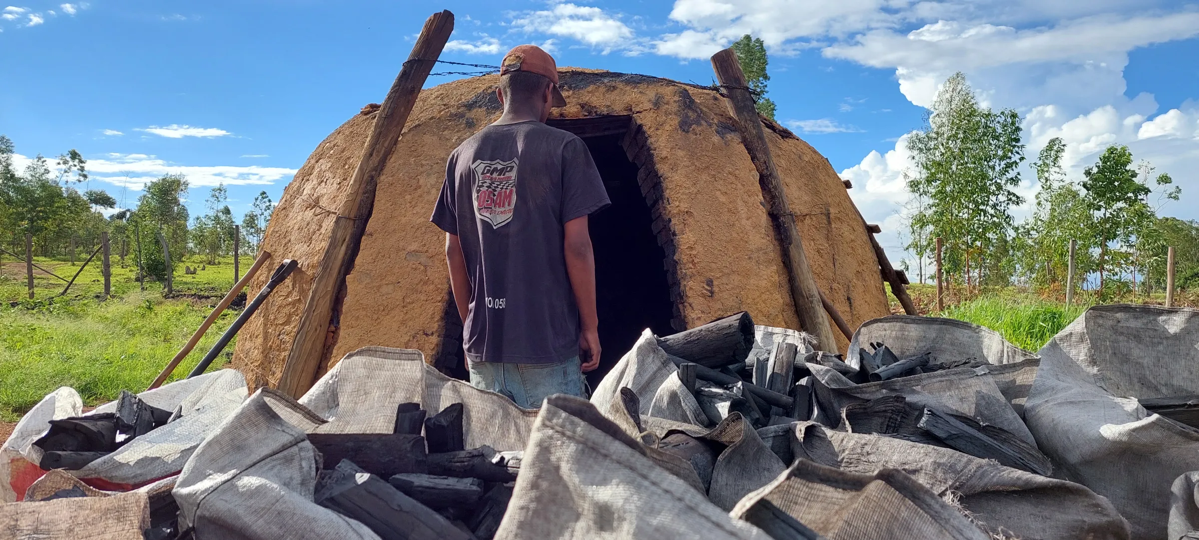 A man stands in front of a kiln behind bags of charcoal