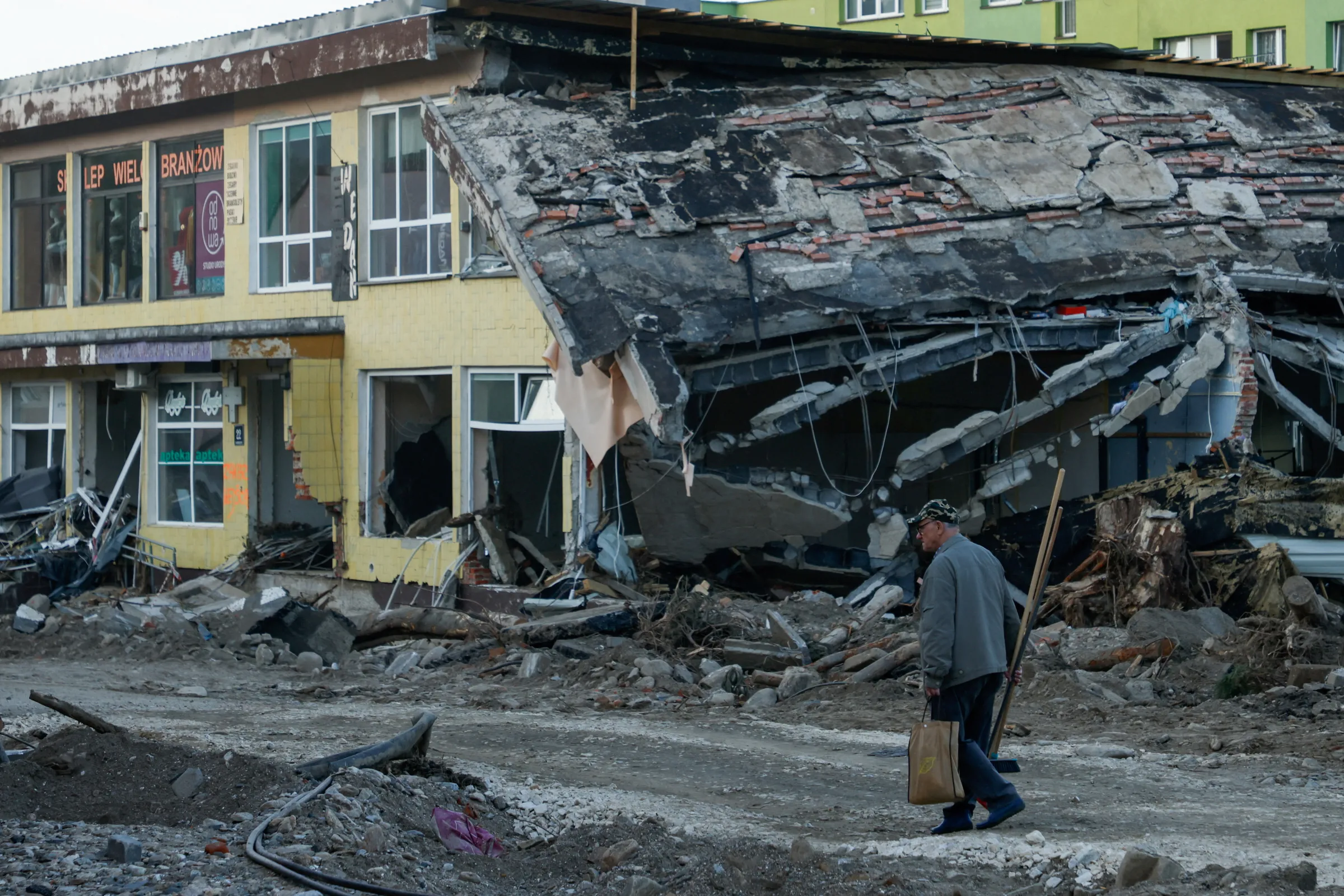 FILE PHOTO: A man with a broom walks by a destroyed building days after intensive flooding in Stronie Slaskie, Poland, September 20, 2024. REUTERS/Kuba Stezycki