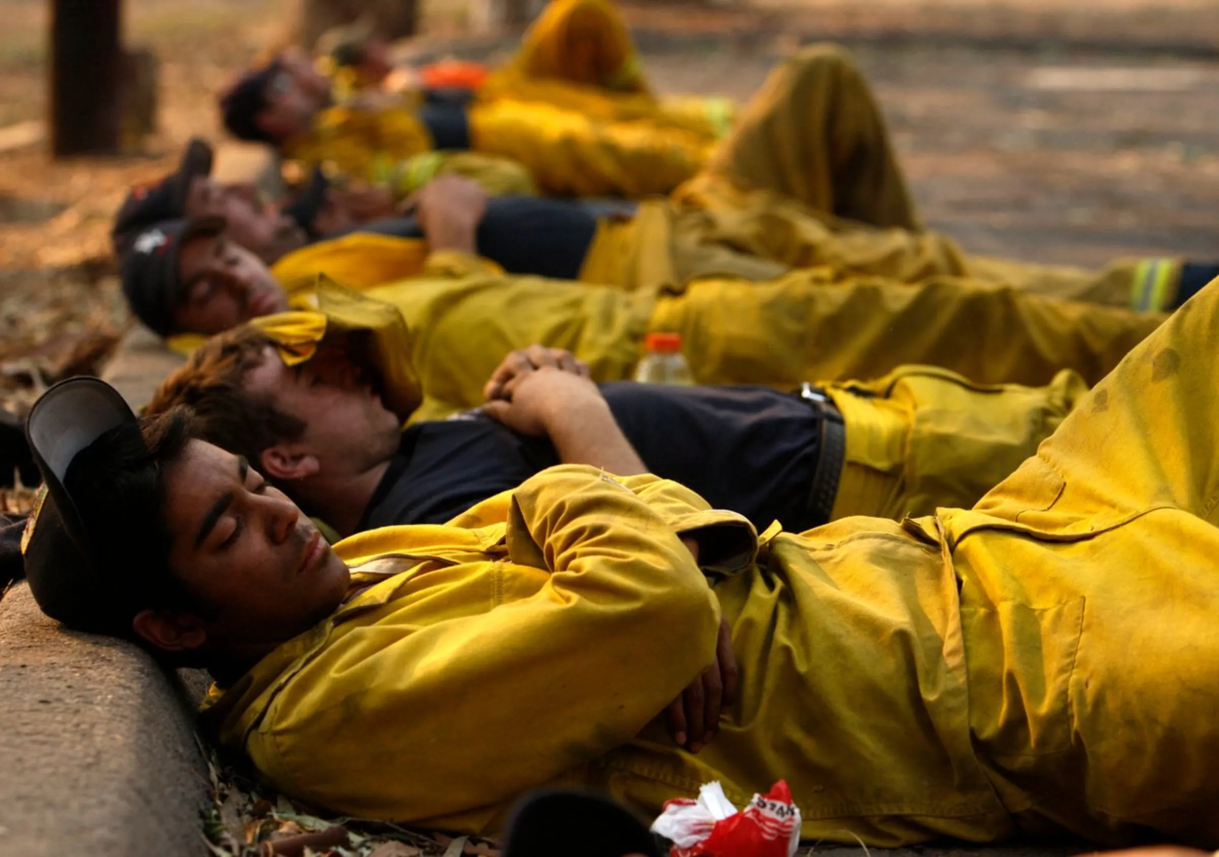 Firefighters sleep by the roadside after fighting fires in Lake Hodges, near San Diego, California, October 23, 2007. Relentless wildfires forcing the largest evacuations in California's modern history raged into a fourth day on Wednesday as 10,000 exhausted firefighters hoped for a break in the hot winds whipping the flames.