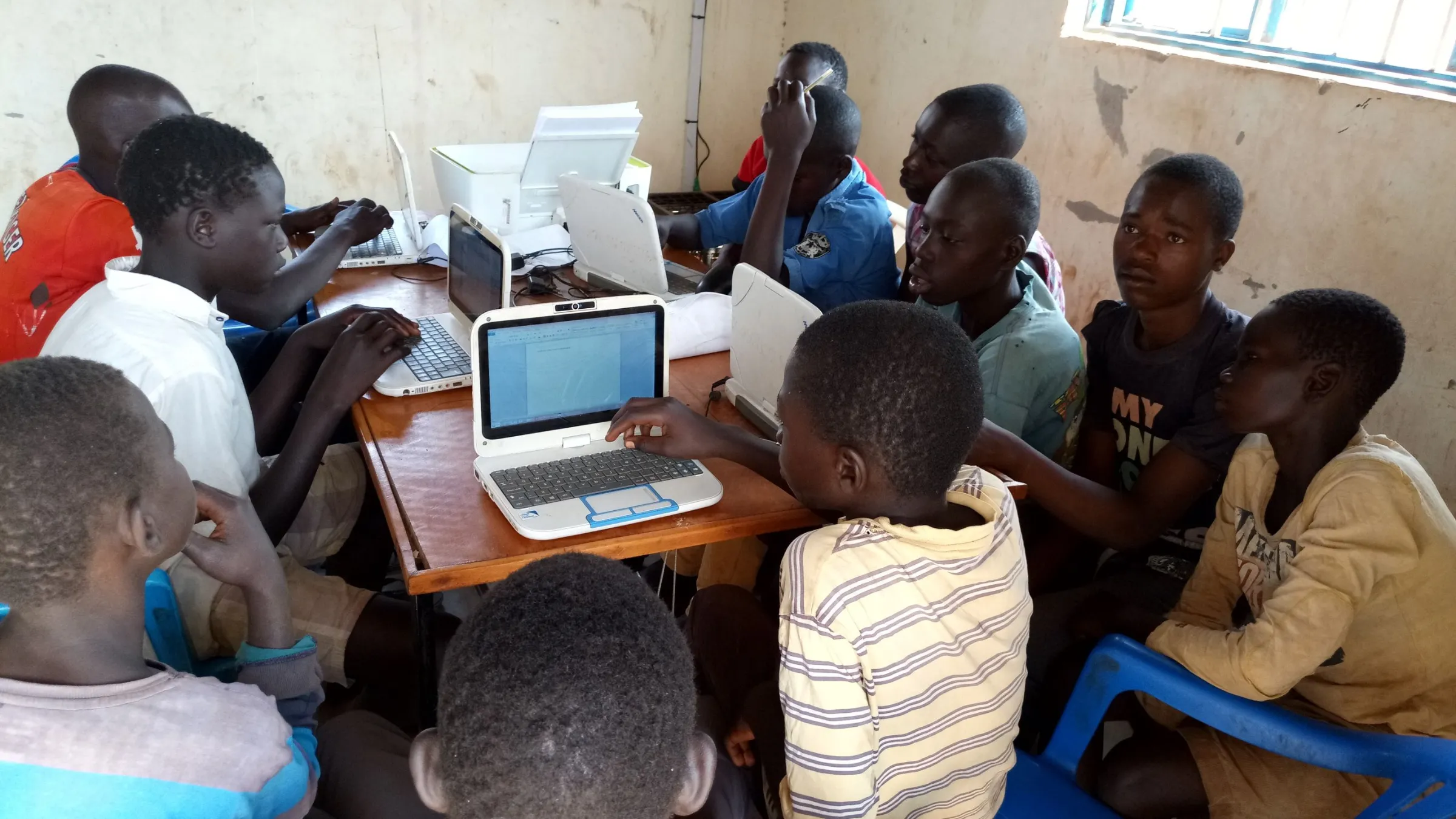 Students gather around computers during ICT training for South Sudanese refugees in the West Nile region in Northern Uganda. Thomson Reuters Foundation/Handout courtesy of BOSCO