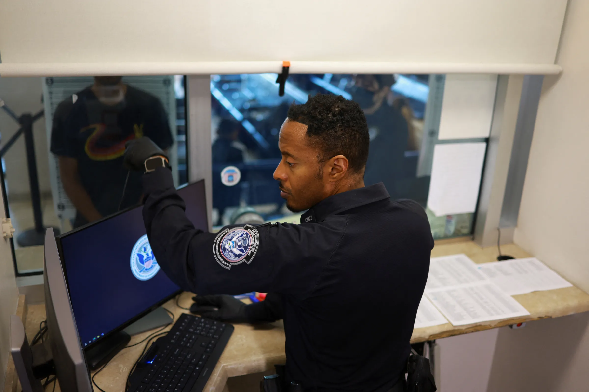 A Customs and Border Protection (CBP) officer works, as a migrant, seeking asylum in the United States and who previously requested an appointment on the U.S. CBP One application, stands, at the CBP building, in El Paso, Texas, U.S. June 14, 2024. REUTERS/Jose Luis Gonzalez