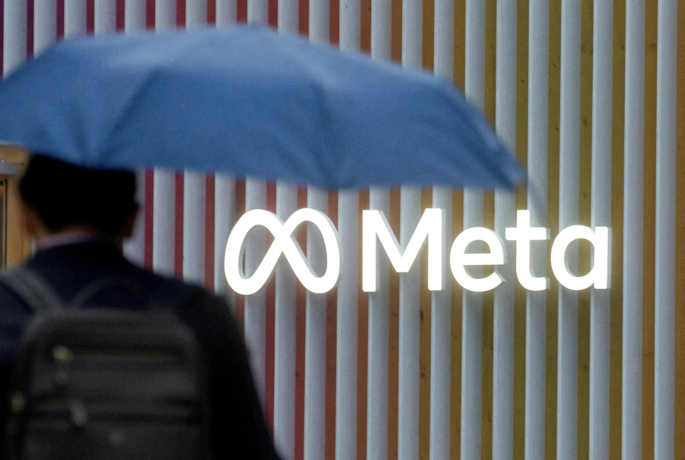 A man holding an umbrella walks past the logo of Meta Platforms seen in Davos, Switzerland, May 22, 2022. REUTERS/Arnd Wiegmann
